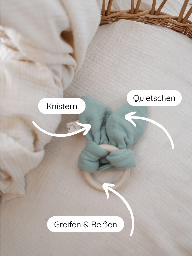 Baby Beißring Baumwoll-Musselin - Mint auf einer Decke: Holzring mit grünen Stoffohren, die knistern und quietschen. Ideal zum Greifen und Beißen, fördert sensorische Entwicklung und Zahnungshilfe.