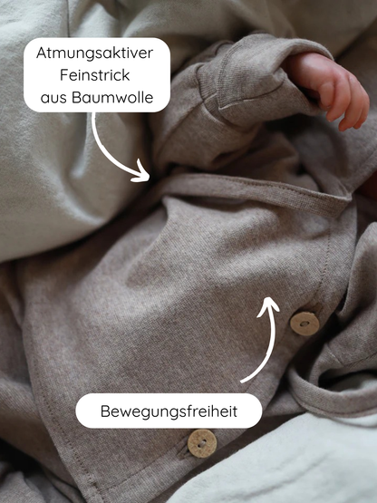 Babyschlüttli Feinstrick - Hafer Meliert: Nahaufnahme eines Babys in einem weichen, atmungsaktiven Feinstrick-Baumwollanzug mit Holzknöpfen und Wickelverschluss, der Bewegungsfreiheit und Komfort bietet.
