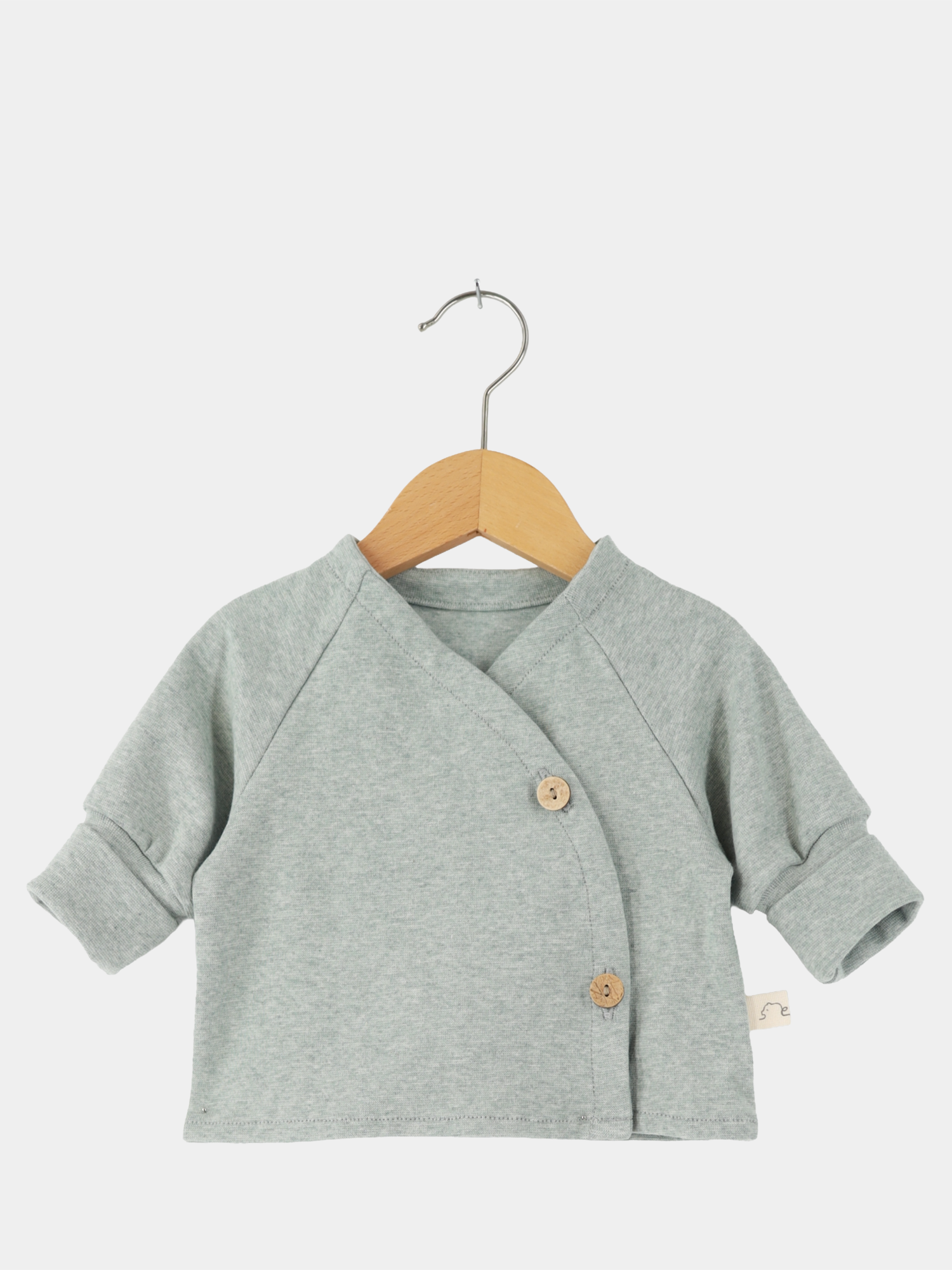 Babyschlüttli Feinstrick - Mint Meliert: Langarm-Wickelshirt aus meliertem Feinstrick-Jersey, mit zwei seitlichen Holzknöpfen. Sanft und anschmiegsam, präsentiert auf einem Holzkleiderbügel. Perfekt für Neugeborene, nachhaltig gefertigt in Berlin.
