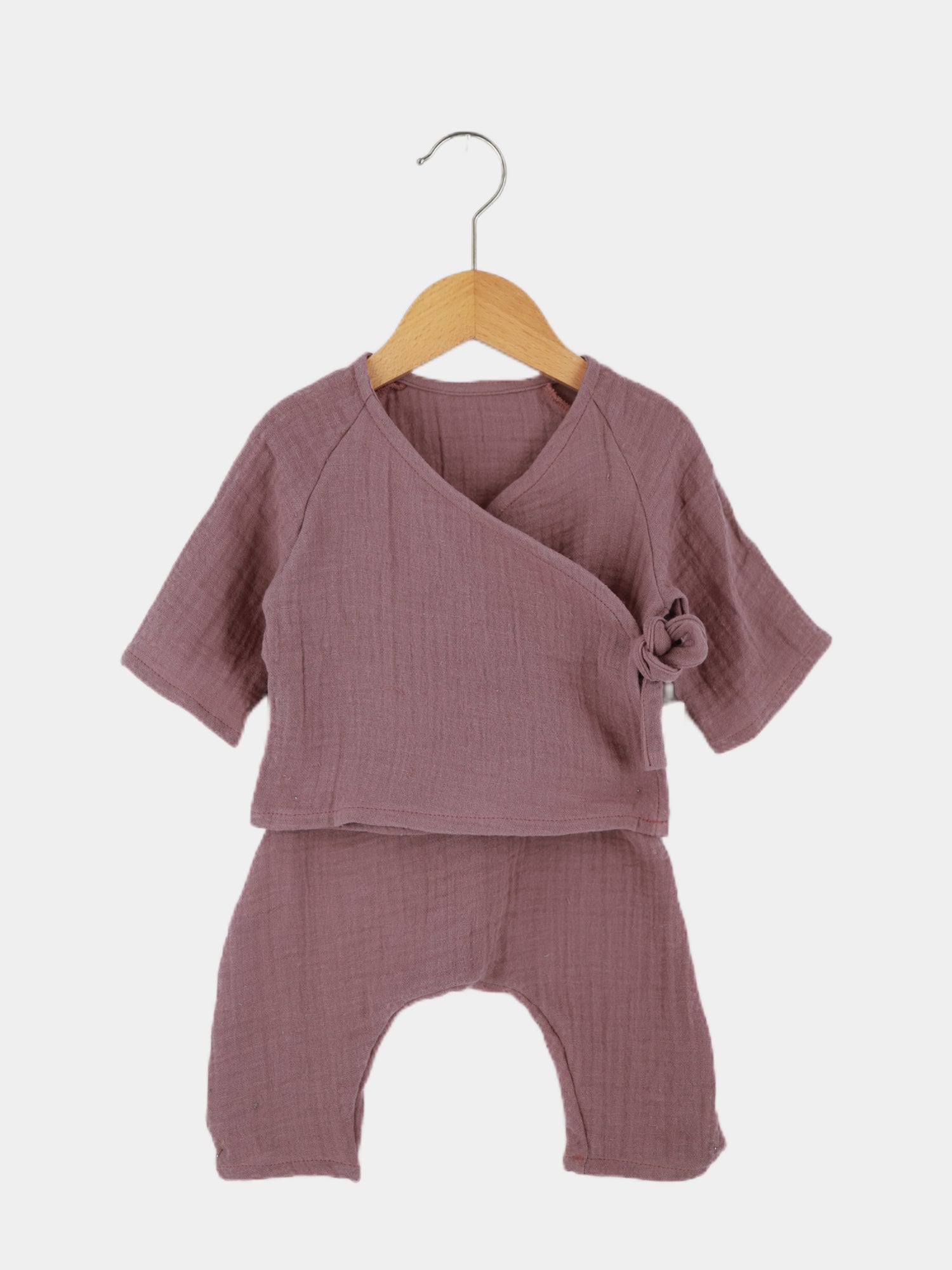 Babyset Baumwoll-Musselin - Malve auf einer Holzschaukel: Ein Wickel-Schlüttli mit seitlicher Schleife und weiten Hosen aus ÖKOTEX-zertifiziertem Musselin, ideal für empfindliche Babyhaut und warmes Wetter.