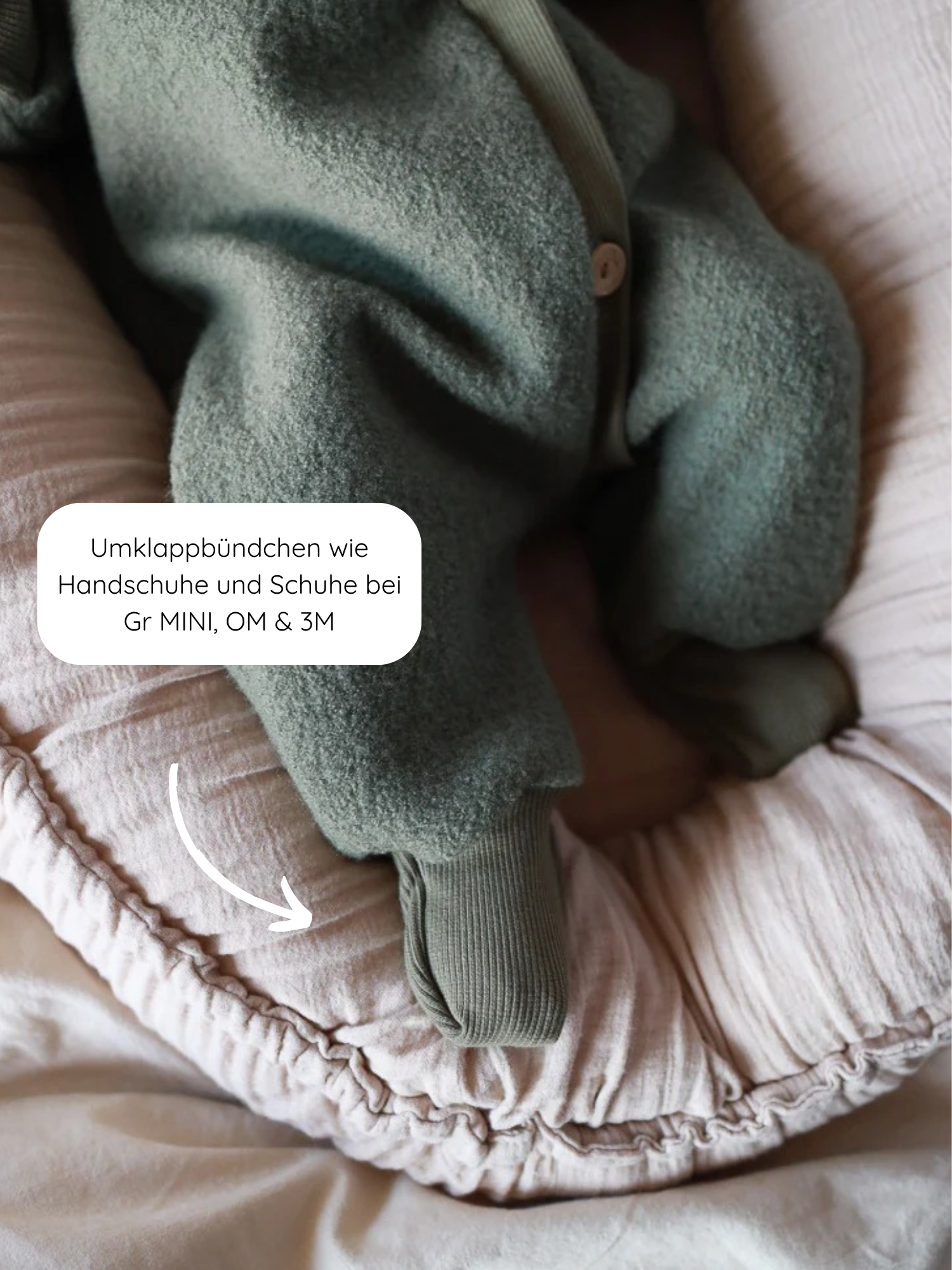 Baby in einem Kuschelanzug Wollwalk - Pistazie aus 100% Schurwolle mit Baumwollfutter, ausgestattet mit umklappbaren Bündchen, ruht auf einem rosa Nestkissen. Perfekt für Frühling bis Winter.