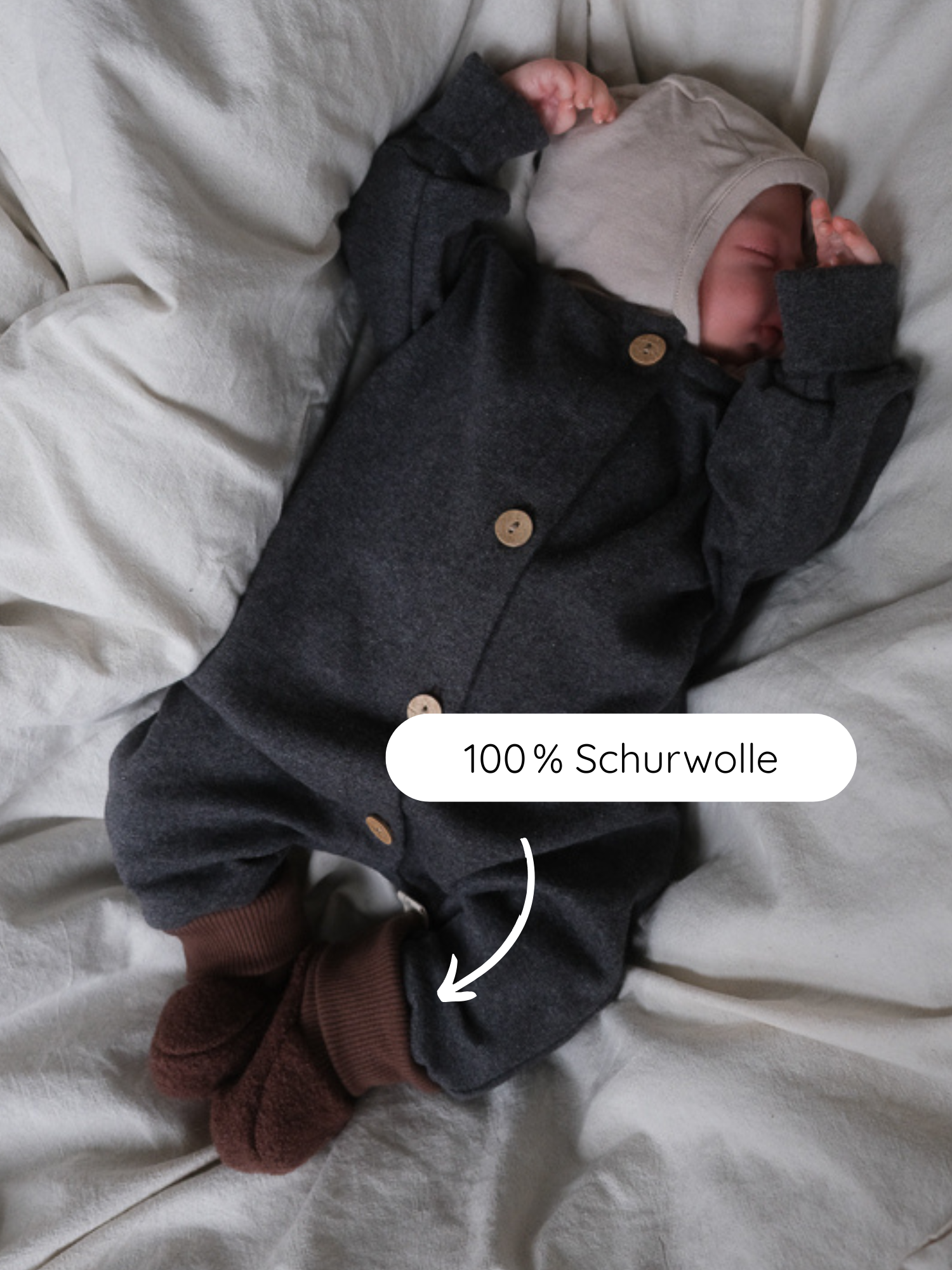 Ein schlafendes Baby trägt einen dunkelgrauen Wollstrampler mit braunen Babybooties Wollwalk - Schoko. Die handgenähten Booties bieten Wärme und Schutz mit elastischen Bündchen für optimalen Halt.