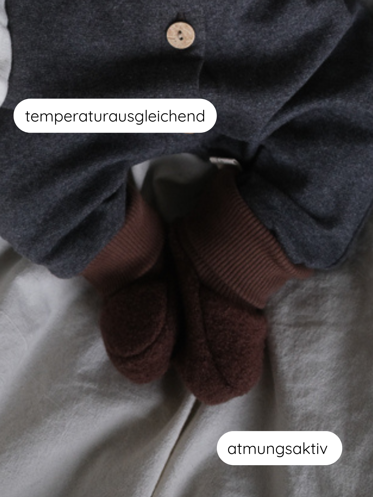 Babybooties Wollwalk - Schoko: Ein kleines Kind trägt dunkle graue Hosen und flauschige braune Wollwalk-Booties mit elastischen Bündchen auf hellen Untergrund. Labels heben „temperaturausgleichend“ und „atmungsaktiv“ hervor.