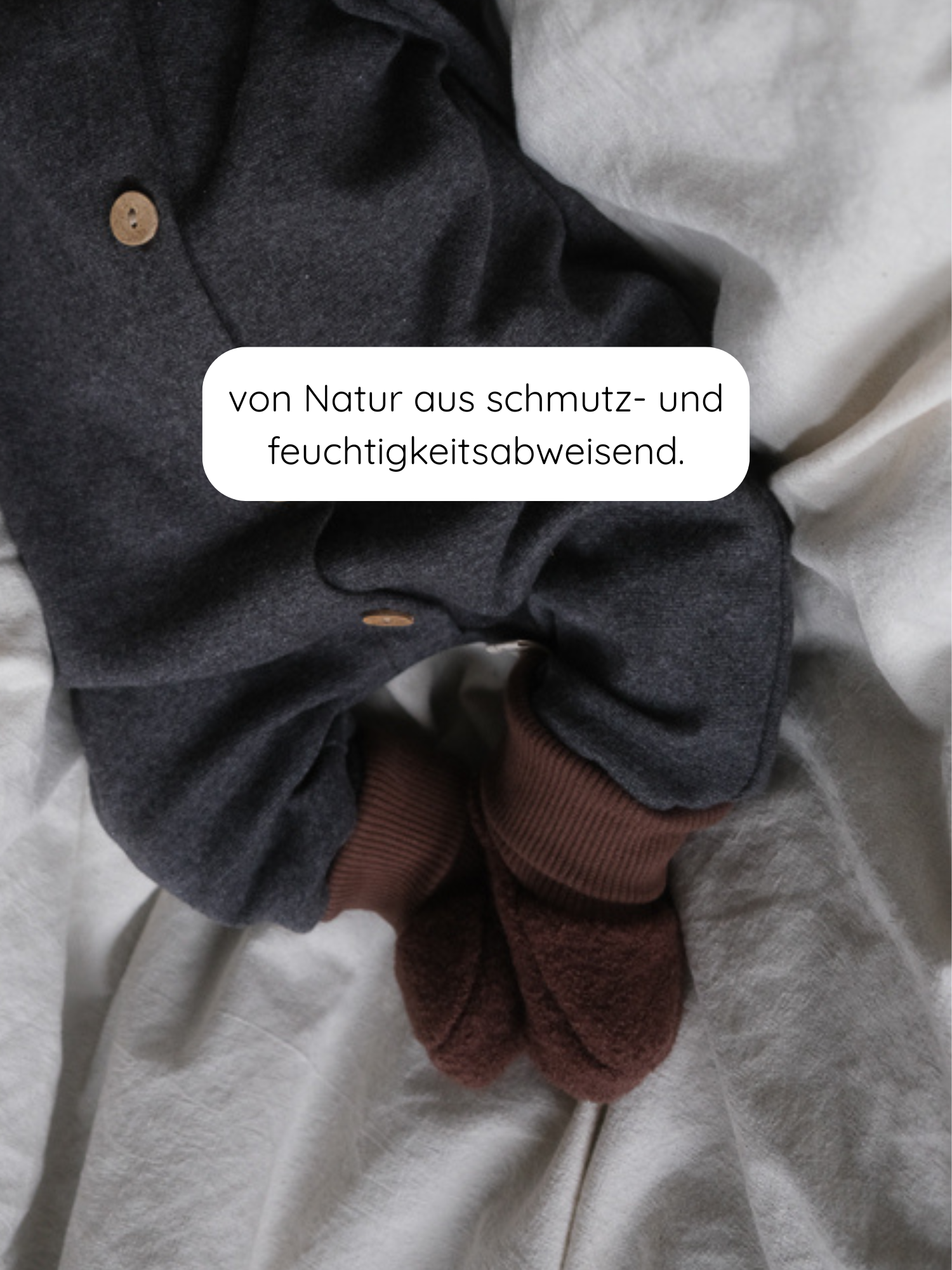 Babybooties Wollwalk - Schoko: Ein dunkelgrauer Babystrampler mit Holzknöpfen, braunen Bündchen und Fußteilen, untermalt mit dem Text von Natur aus schmutz- und feuchtigkeitsabweisend.