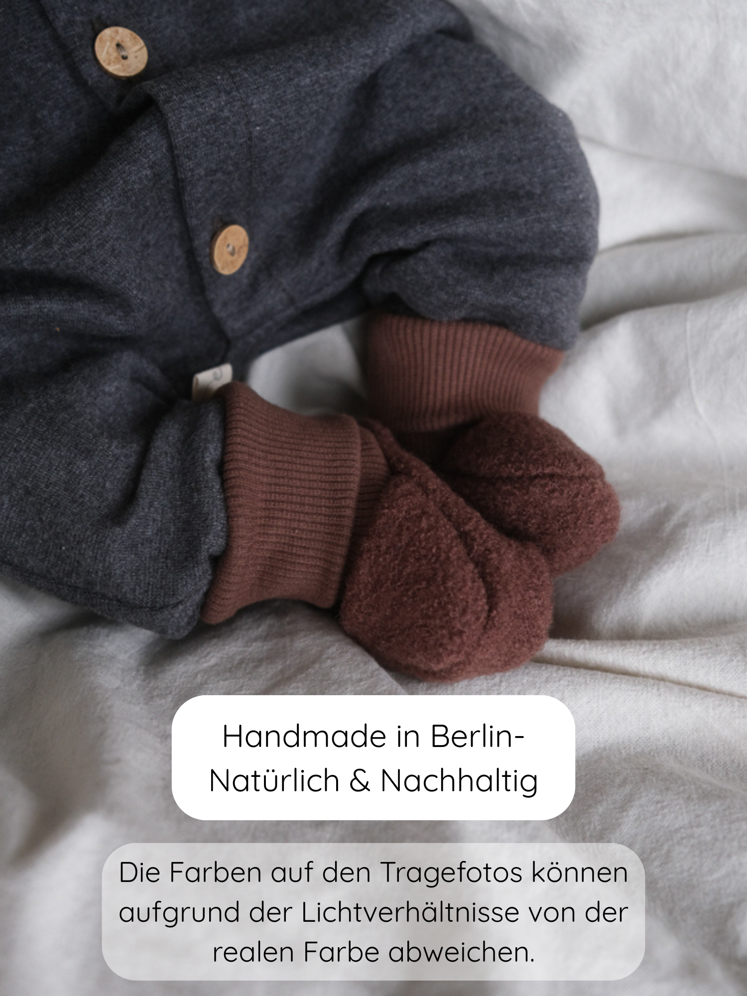 Nahaufnahme eines Babys in einem dunkelgrauen Strampler mit braunen Bündchen und Babybooties Wollwalk - Schoko. Handgefertigt in Berlin aus gewalkter Schurwolle mit elastischen Jersey-Bündchen für optimalen Halt.