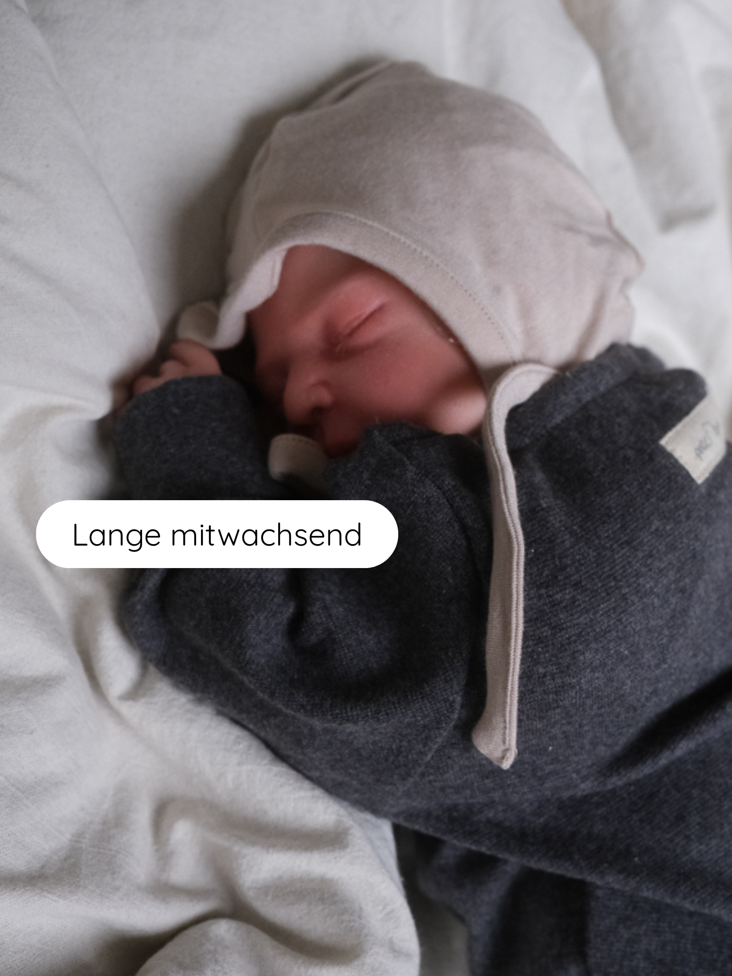 Schlafendes Neugeborenes auf weicher Decke, trägt ein Babyhäubchen Kaschmir-Mix - Sand. Das elastische, kuschelweiche Mützchen mit langen Bändern bietet Wärme und wächst mit.