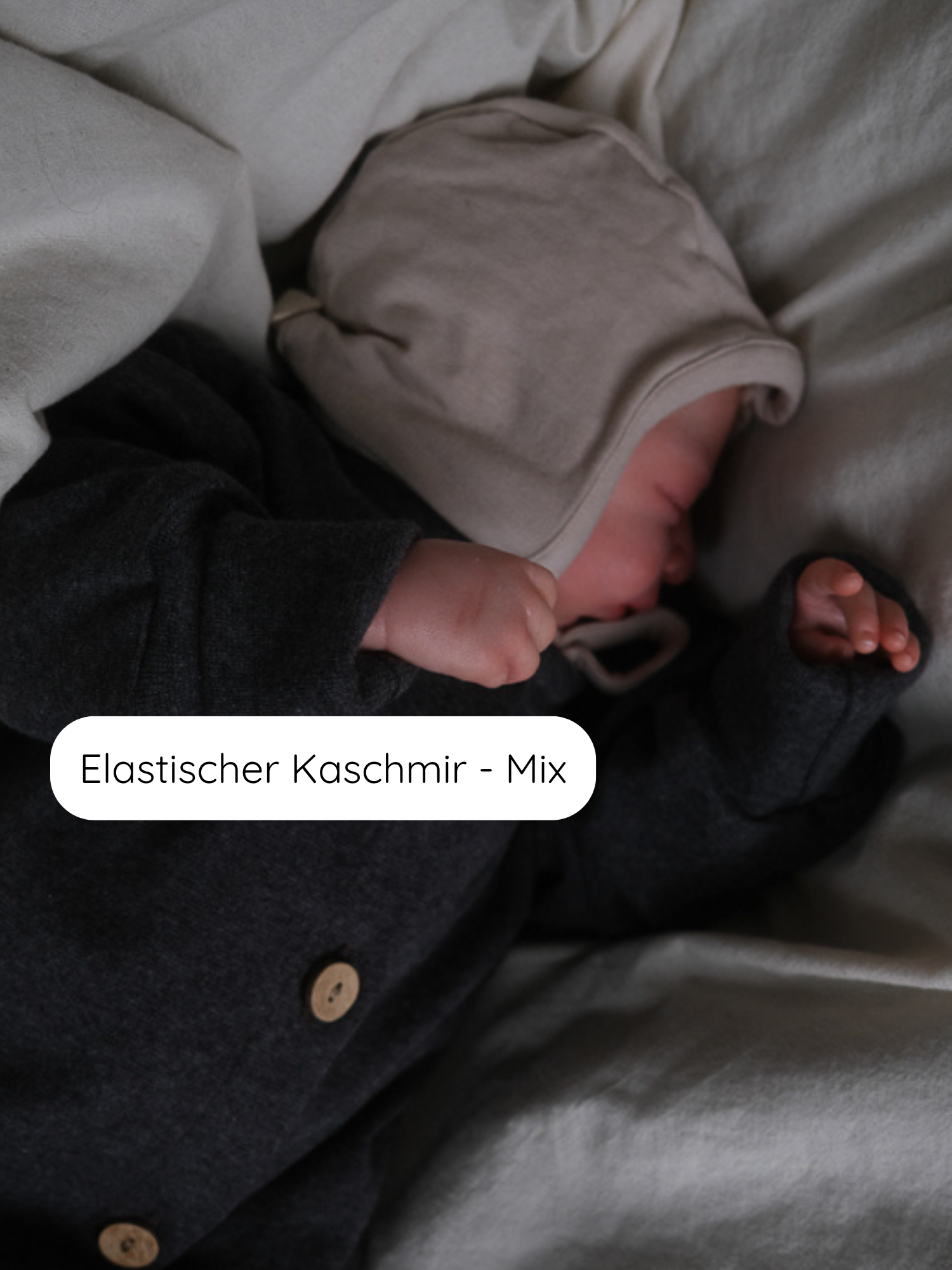 Ein schlafendes Baby trägt einen zweifarbigen Strick-Loopbody mit Kapuze. Der Babyhäubchen Kaschmir-Mix - Sand, passend dazu, bietet Wärme und Schutz aus elastischem Cashmere-Mix-Stoff.