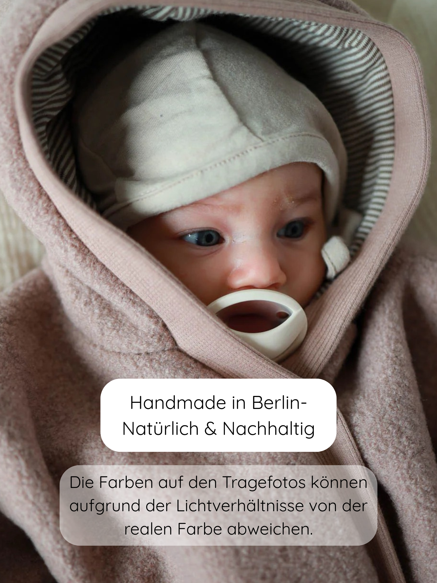 Baby lächelt geborgen im Babyhäubchen Kaschmir-Mix - Sand, handgefertigt in Berlin. Die weiche, elastische Haube bietet Wärme und Schutz, perfekt ergänzt durch den Loopbody Kaschmir-Mix.