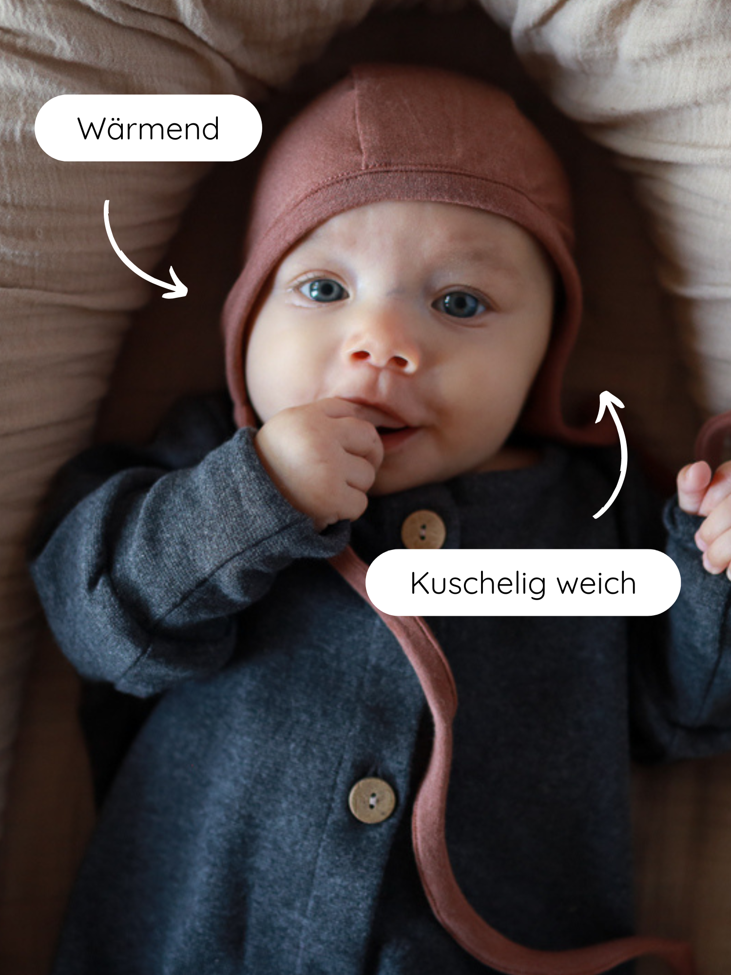 Babyhäubchen Kaschmir-Mix - Zimt auf einem Baby, das in einem Nest liegt. Das Häubchen bietet Wärme und Schutz, ist elastisch und passt perfekt zum kuschelig-weichen, dunkelgrauen Loopbody.