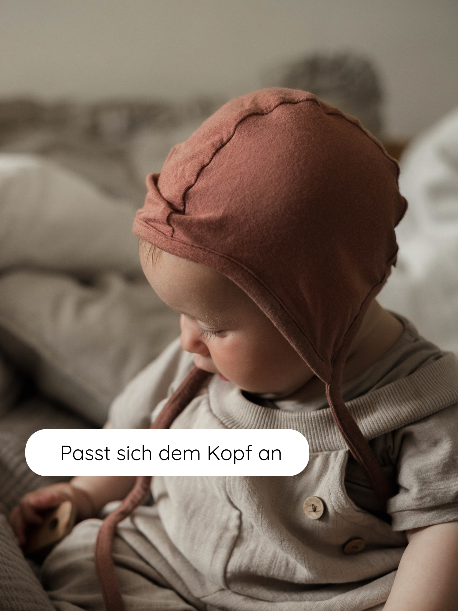 Ein Baby trägt das Babyhäubchen Kaschmir-Mix - Zimt, das sich sanft an den Kopf schmiegt. Die Mütze bietet Wärme und Schutz, ideal für empfindliche Babyköpfchen.