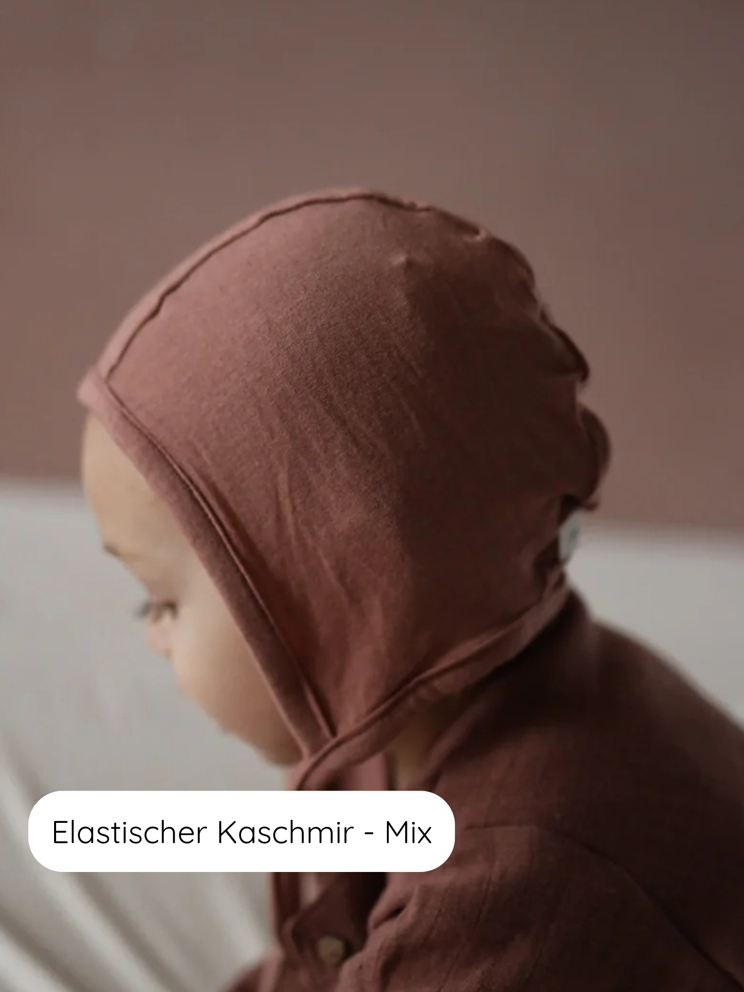 Babyhäubchen Kaschmir-Mix - Zimt: Ein Baby trägt ein weiches, braunes Strickhäubchen aus elastischem Kaschmir-Mix, das sanft am Kopf anliegt. Ideal für Wärme und Schutz mit langen Bindebändern.