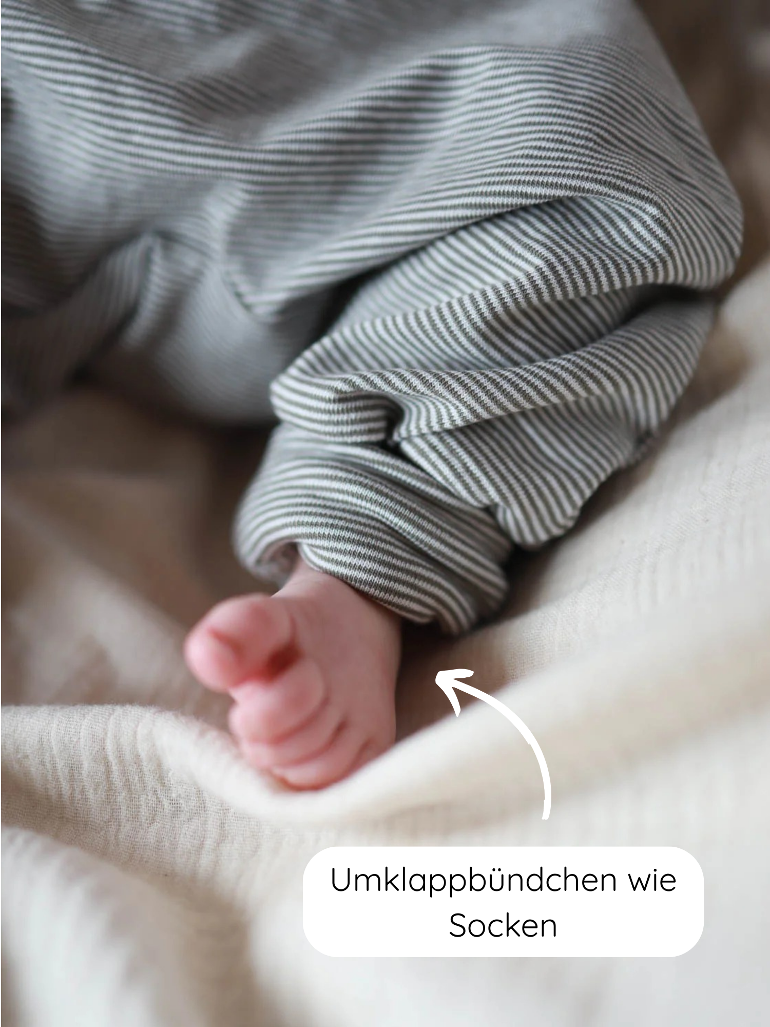 Nahaufnahme eines Babyfußes, der aus gestreiften Babyknicker Bio-Baumwolle - Maus Ringel hervorlugt, mit umklappbaren Bündchen an den Beinen, die wie eingebaute Socken wirken.