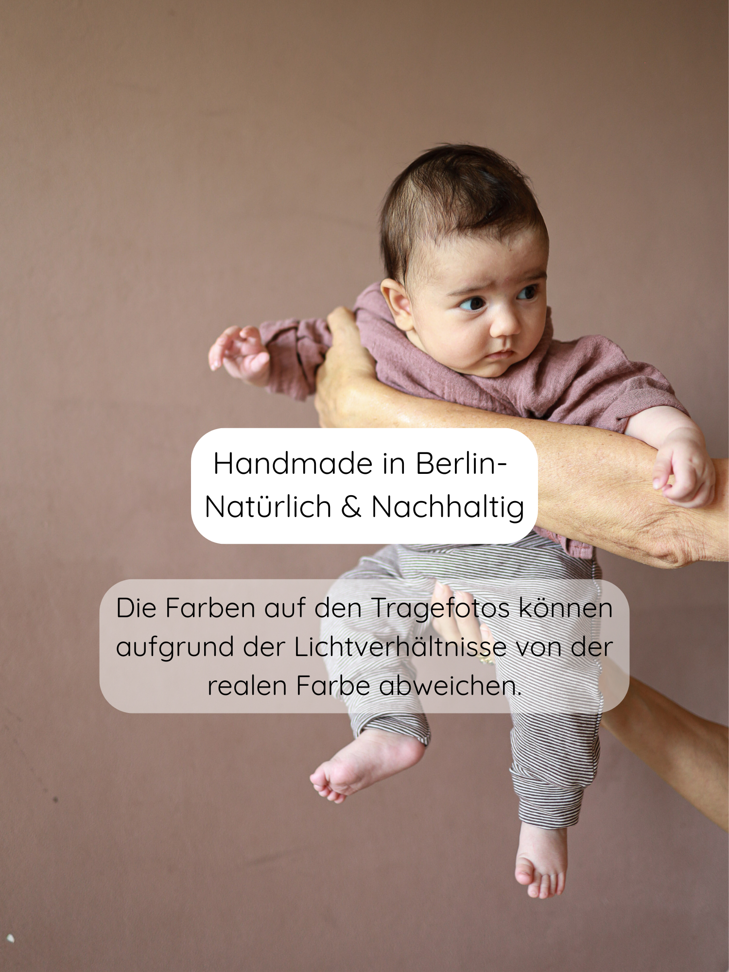 Baby in Babyknicker Bio-Baumwolle - Schoko Ringel, gehalten vor warmem Hintergrund. Text betont handgefertigt, natürlich, nachhaltig in Berlin. Hinweis auf mögliche Farbabweichungen durch Lichtverhältnisse.