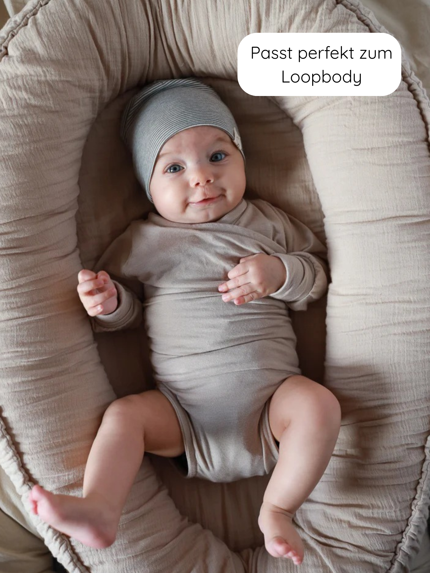 Säugling liegt in einem kuscheligen Nest, trägt einen Beanie Bio-Baumwolle - Ringel Maus in neutralem Beige, perfekt passend zum Loopbody, mit klassischem, zeitlosem Ringelmuster, ideal für empfindliche Haut.