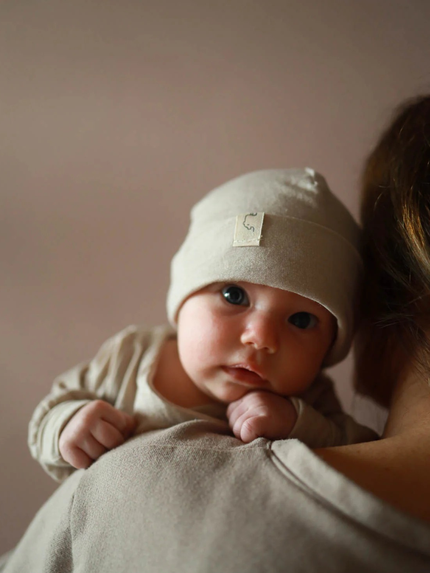 Baby ruht auf Schulter, trägt Beanie Kaschmir-Mix - Sand. Die weiche, dehnbare Mütze passt sich optimal an, ideal für empfindliche Babyhaut, handgemacht in Berlin.