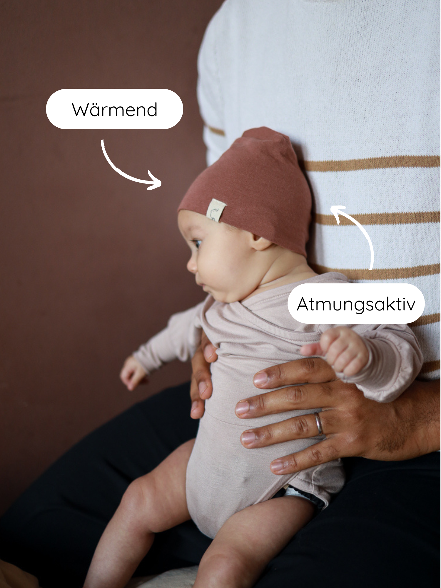 Beanie Kaschmir-Mix - Zimt: Ein Baby mit zimtfarbener Kaschmir-Mix-Mütze sitzt auf einem Schoß. Die Mütze ist wärmend und passt sich dem Kopf sanft an.