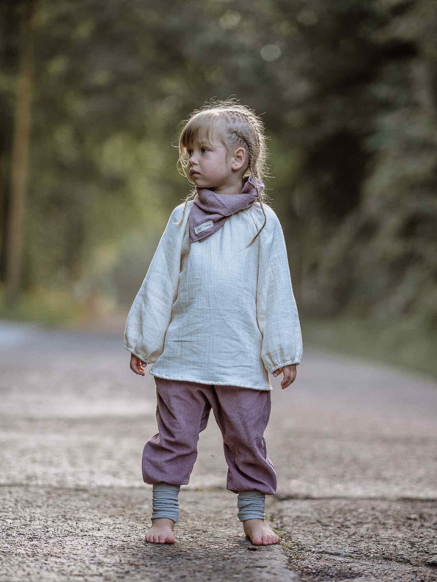 Kleinkind trägt das Blüschen Bio-Musselin - Natur: ein locker geschnittenes, langärmliges Oberteil aus weichem Bio-Musselin, ideal für warme Tage. Perfekt für empfindliche Kinderhaut, fair handgemacht in Berlin.