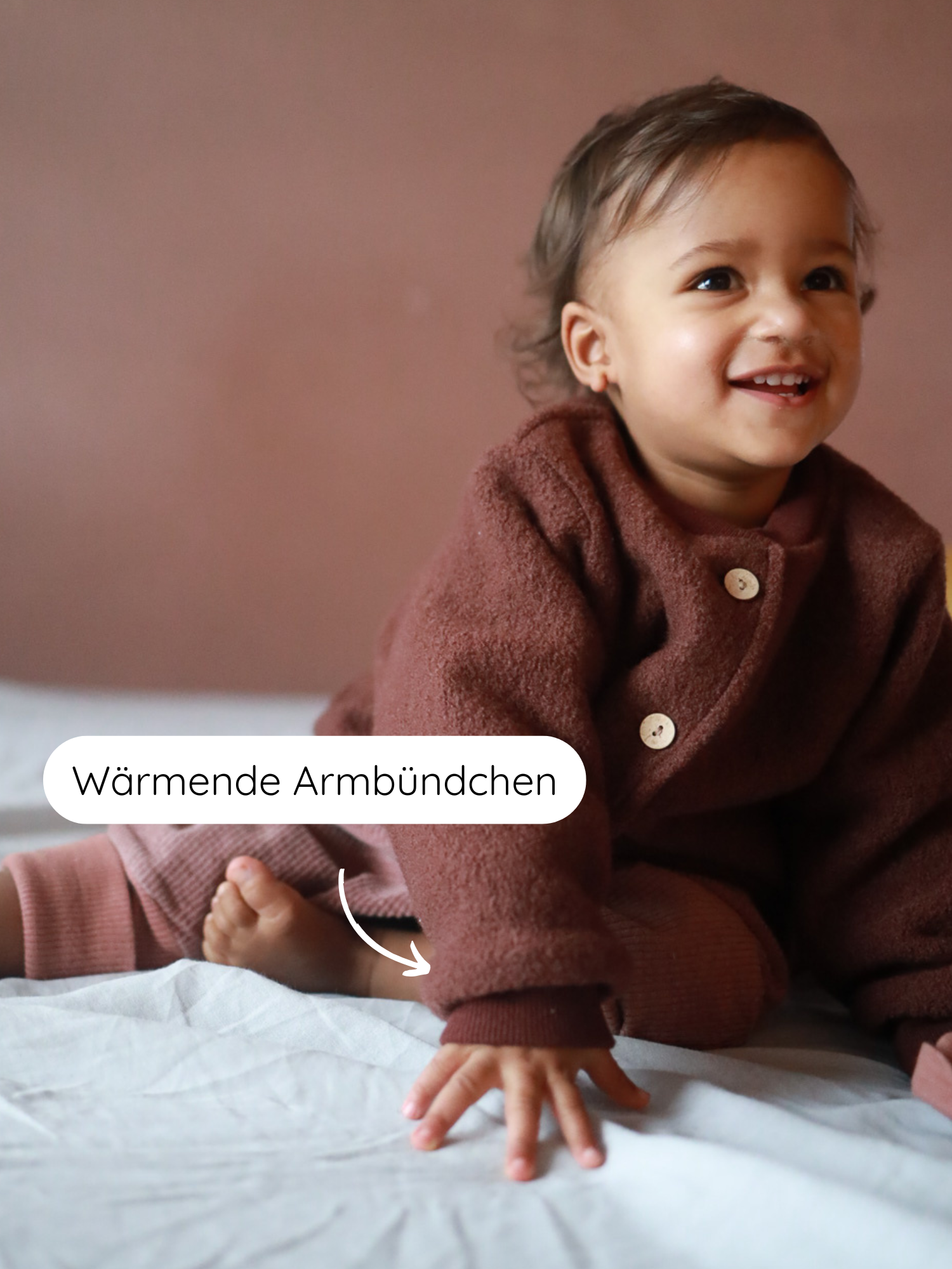 Ein Kleinkind trägt die Bomberjacke Wollwalk - Schoko, zeigt lächelnd die wärmenden Armbündchen. Der Fokus liegt auf den kuscheligen, hochgekrempelten Ärmeln für optimalen Komfort.