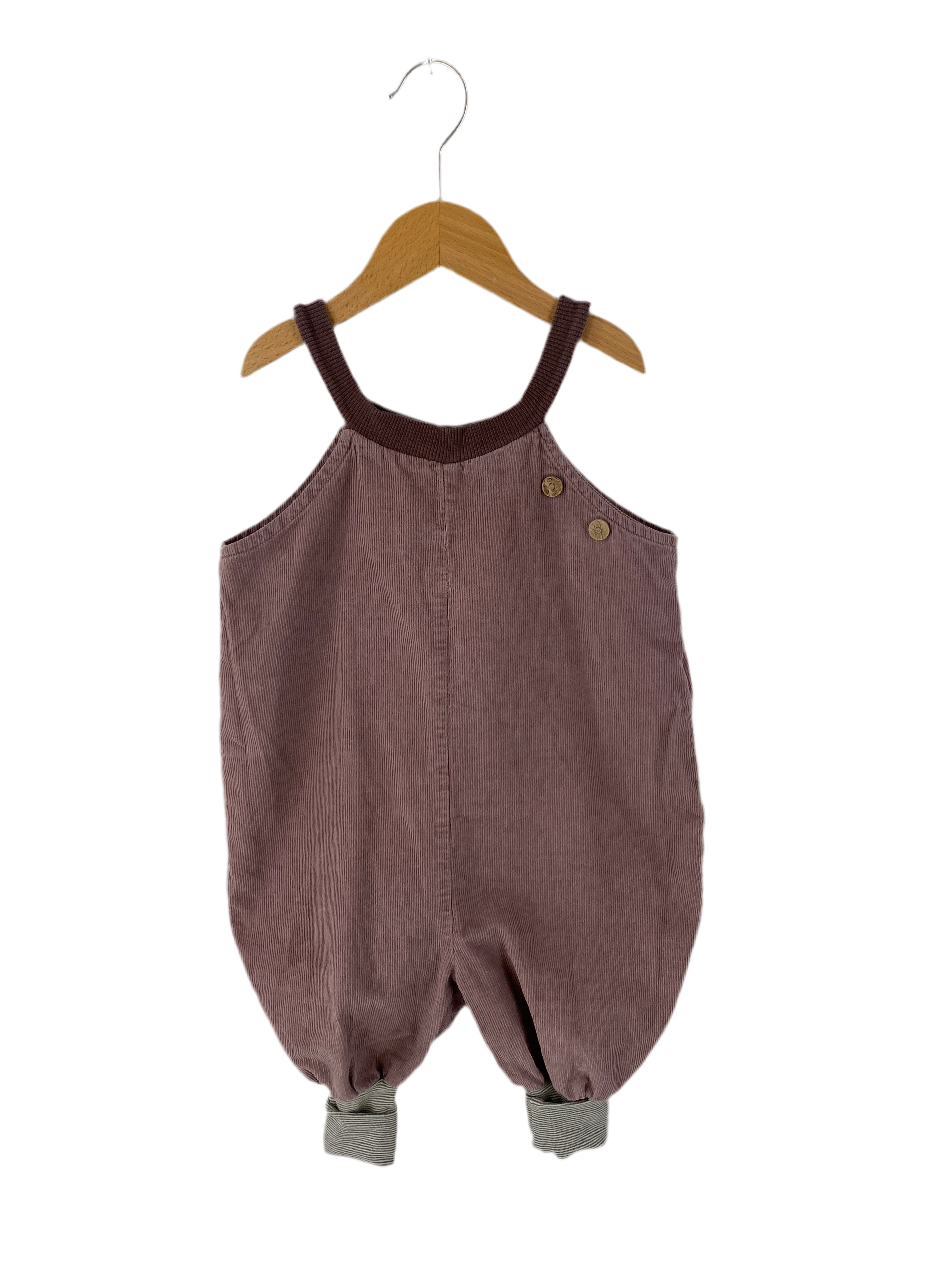(Kopie) Schlupflatzhose Feincord Malve Gr 1Y: Kinder-Cord-Overall in Malve mit breiten Trägern und Holzknöpfen. Beinabschlüsse mit gestreiftem Futter. Hängt an einem Holzkleiderbügel vor weißem Hintergrund. Zustand: gut.
