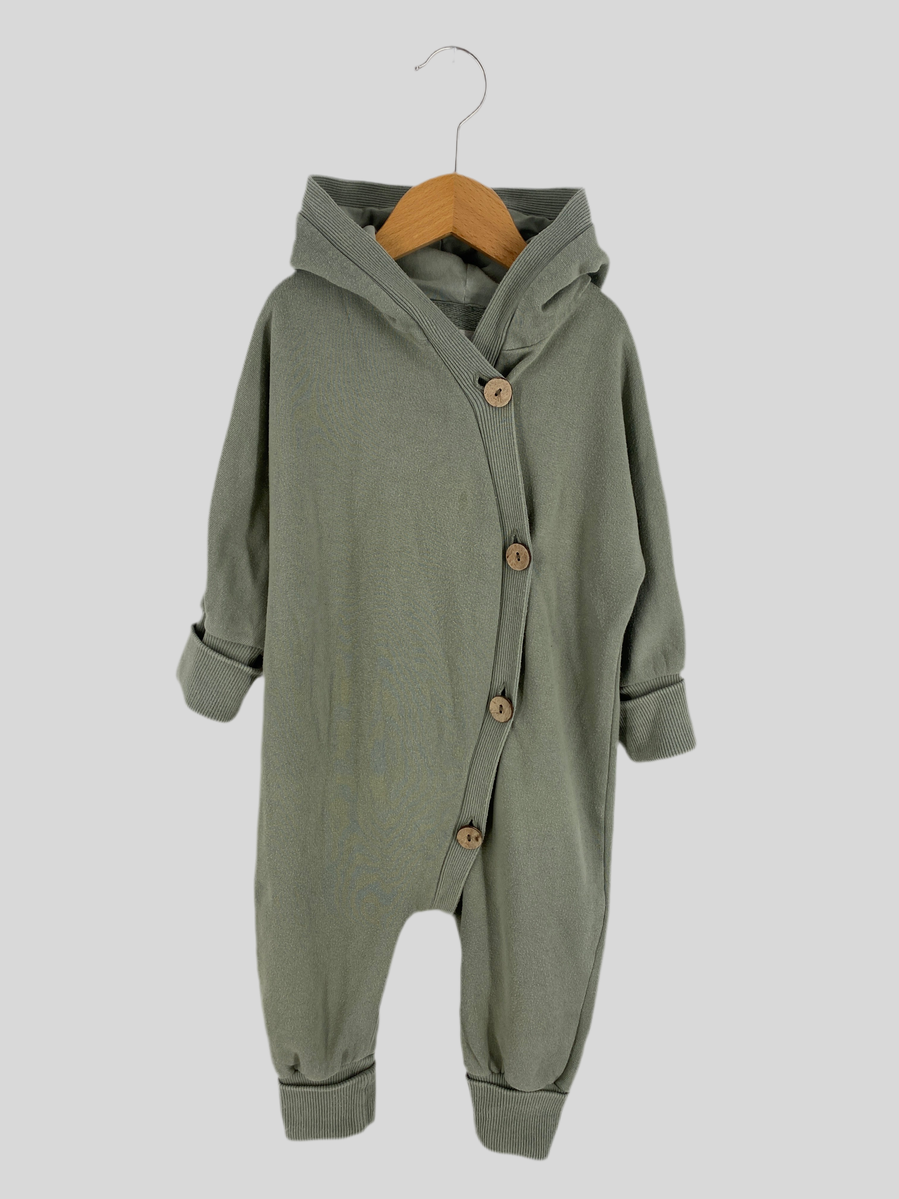 Kopie Kuschelanzug Bio Sweat Aqua Gr 1: Hooded Baby-Romper mit langen Ärmeln, diagonalem Placket mit Holzknöpfen, gerippten Bündchen, präsentiert auf einem Holzkleiderbügel vor neutralem Hintergrund. Zustand: gut.
