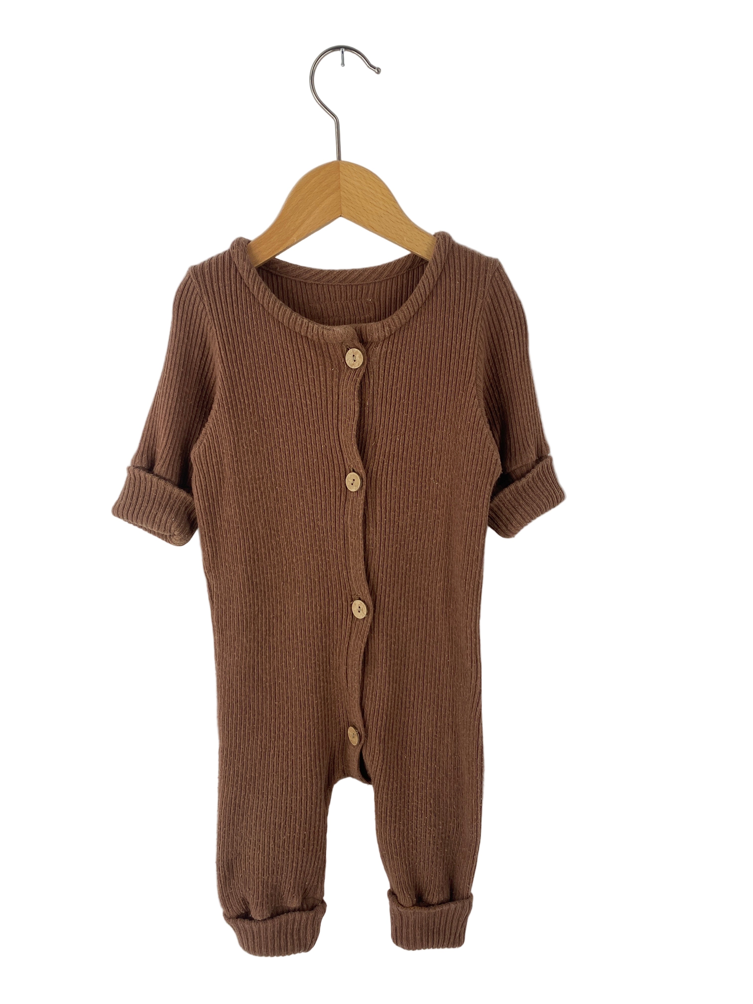 Kopie Mini-Overall Rippstrick Nougat Gr 3M, ein warmer brauner Einteiler aus geripptem Strickstoff, mit Holzknopfleiste, langen Ärmeln und hochgekrempelten Bündchen, hängt an einem Holzbügel. Zustand: sehr gut.