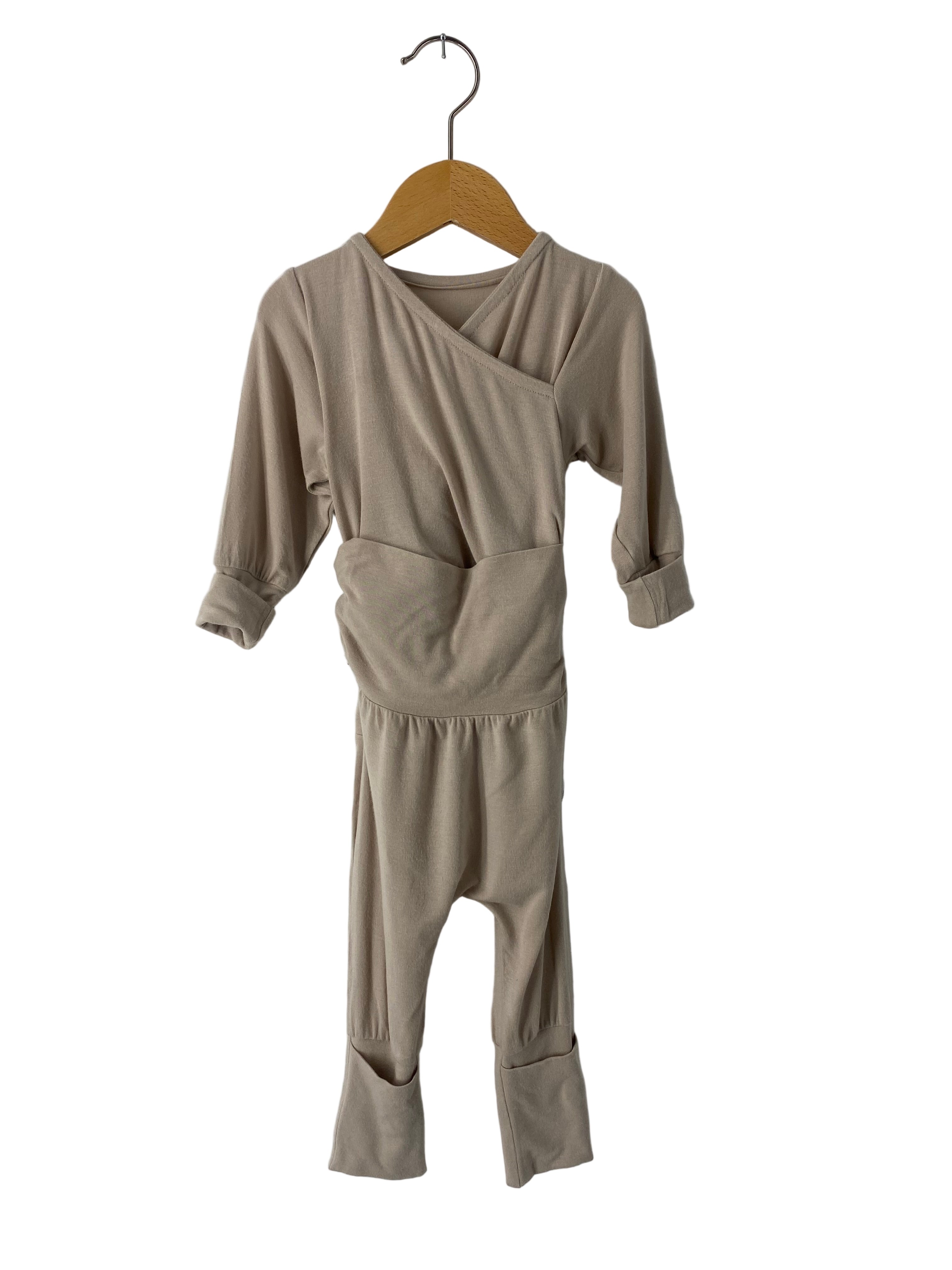 Einzelner Loopstrampler Kaschmir Mix Sand Gr 6M, mit Wickelkragen, langen Ärmeln und Fußstulpen, hängt an einem Holzbügel. Der Zustand ist wie neu, ideal für Babys.