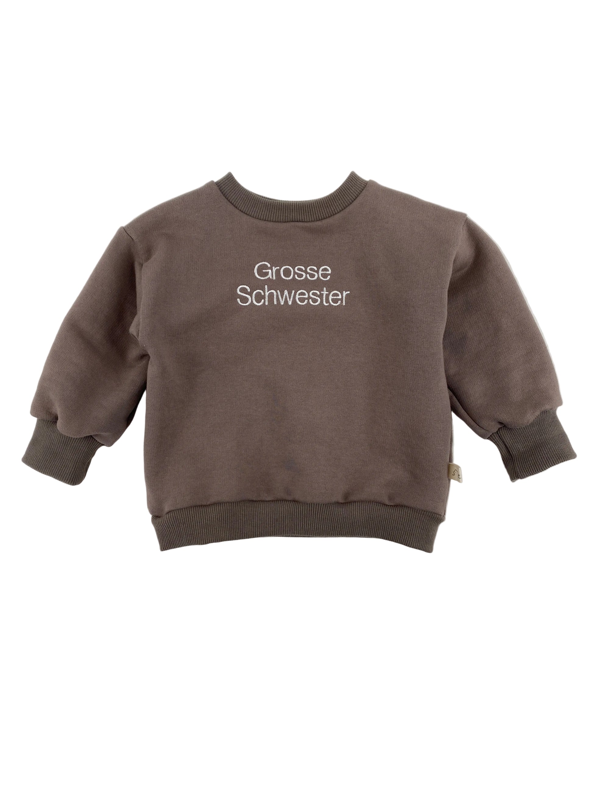 Der Pulli Bio Sweat Praline Gr 1Y zeigt einen kleinen, braunen Crewneck-Sweatshirt mit weißen Stickereien „Grosse Schwester“ vorne, ideal für Kleinkinder, mit gerippten Bündchen und Saum.