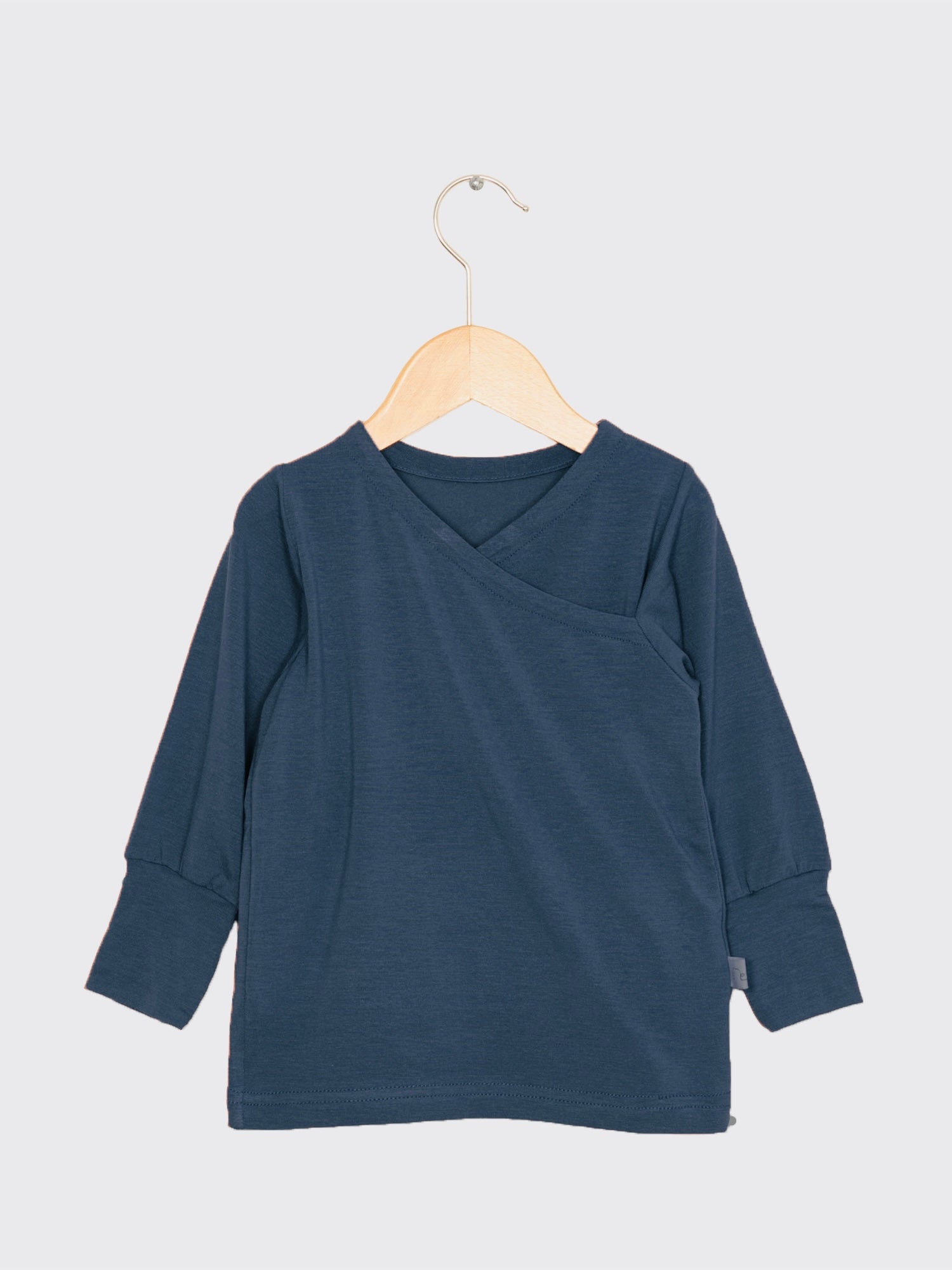 Wickelshirt aus Kaschmir-Mix - Blaubeere: Navyblauer, langärmeliger, kimonoartiger Kinderoberteil an Holzkleiderbügel, aus weichem, elastischem Kaschmir-Micromodal-Mix, handgefertigt in Berlin, atmungsaktiv und temperaturregulierend, mit krempelbaren Bündchen.