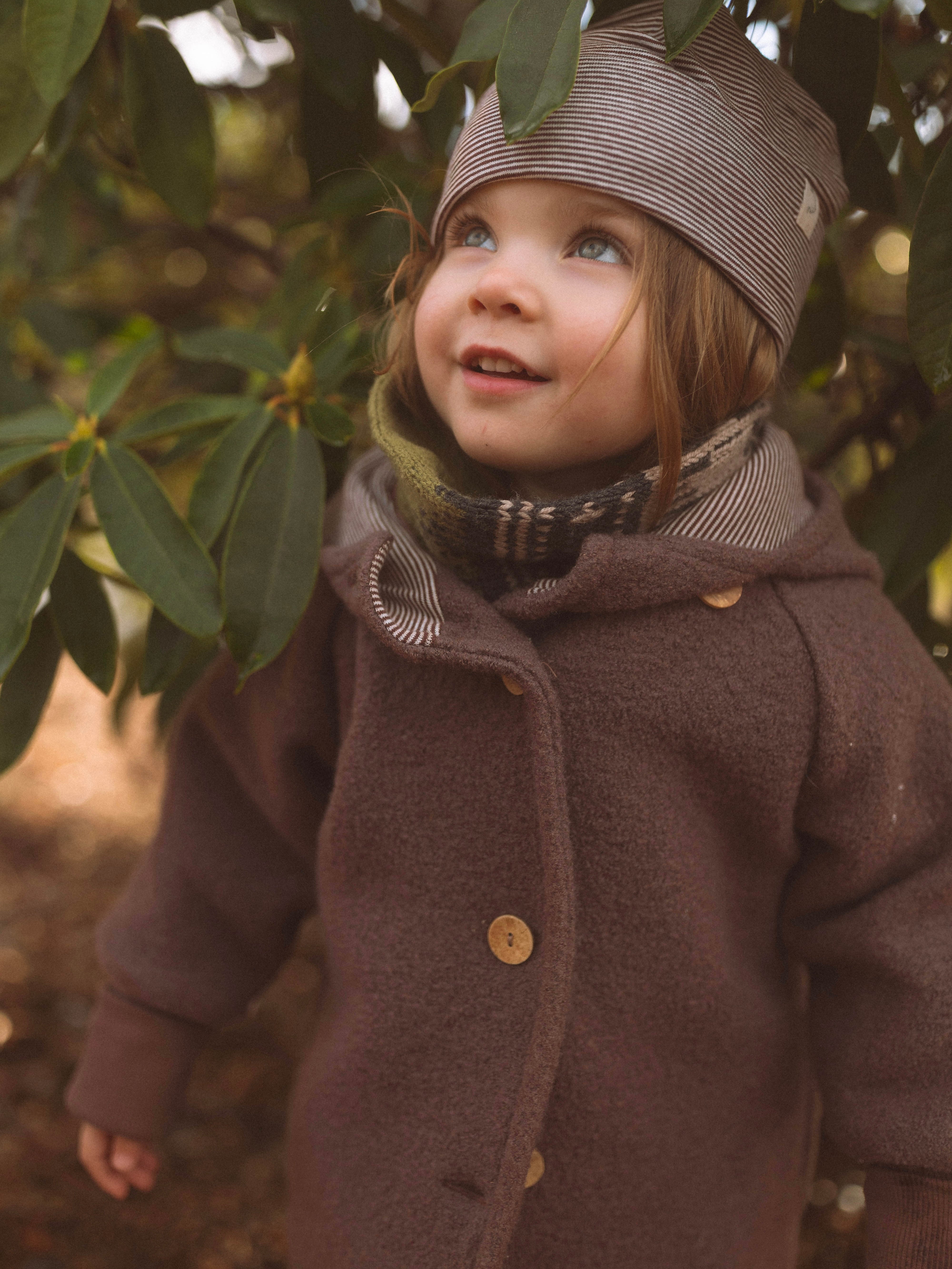 Ein neugieriges Kleinkind trägt die Wichteljacke Wollwalk - Malve, eine warme, gefütterte Jacke mit Bio-Jersey-Futter, ideal für kühle Jahreszeiten, mitwachsend und handgefertigt in Berlin.