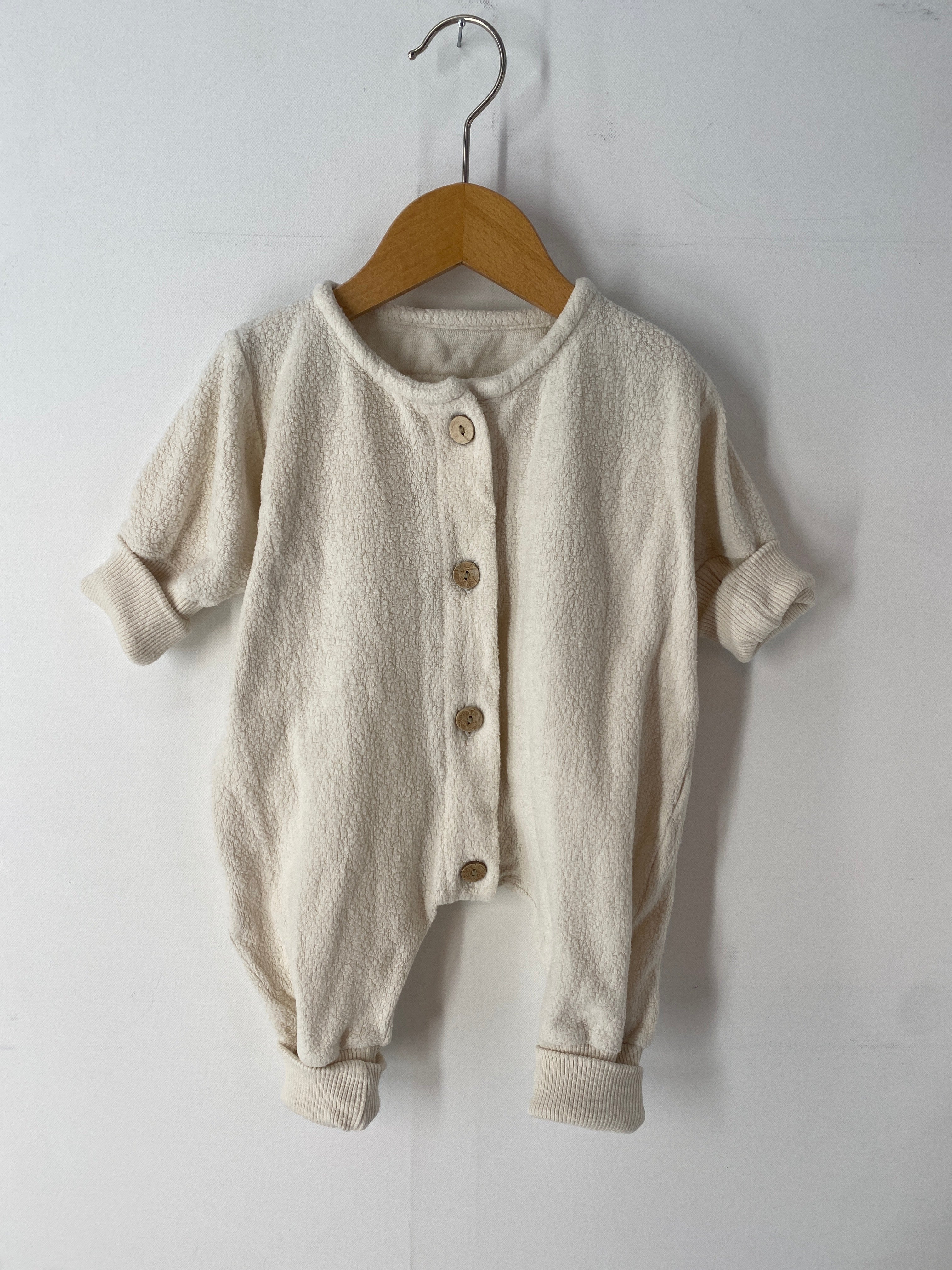 Overall Bio-Teddy Natur Gr 0M auf einem Holzschaukelstuhl, detaillierte Ansicht eines weißen Strickstoffes und Knopfes, präsentiert auf einem Kleiderbügel. Zustand: sehr gut.