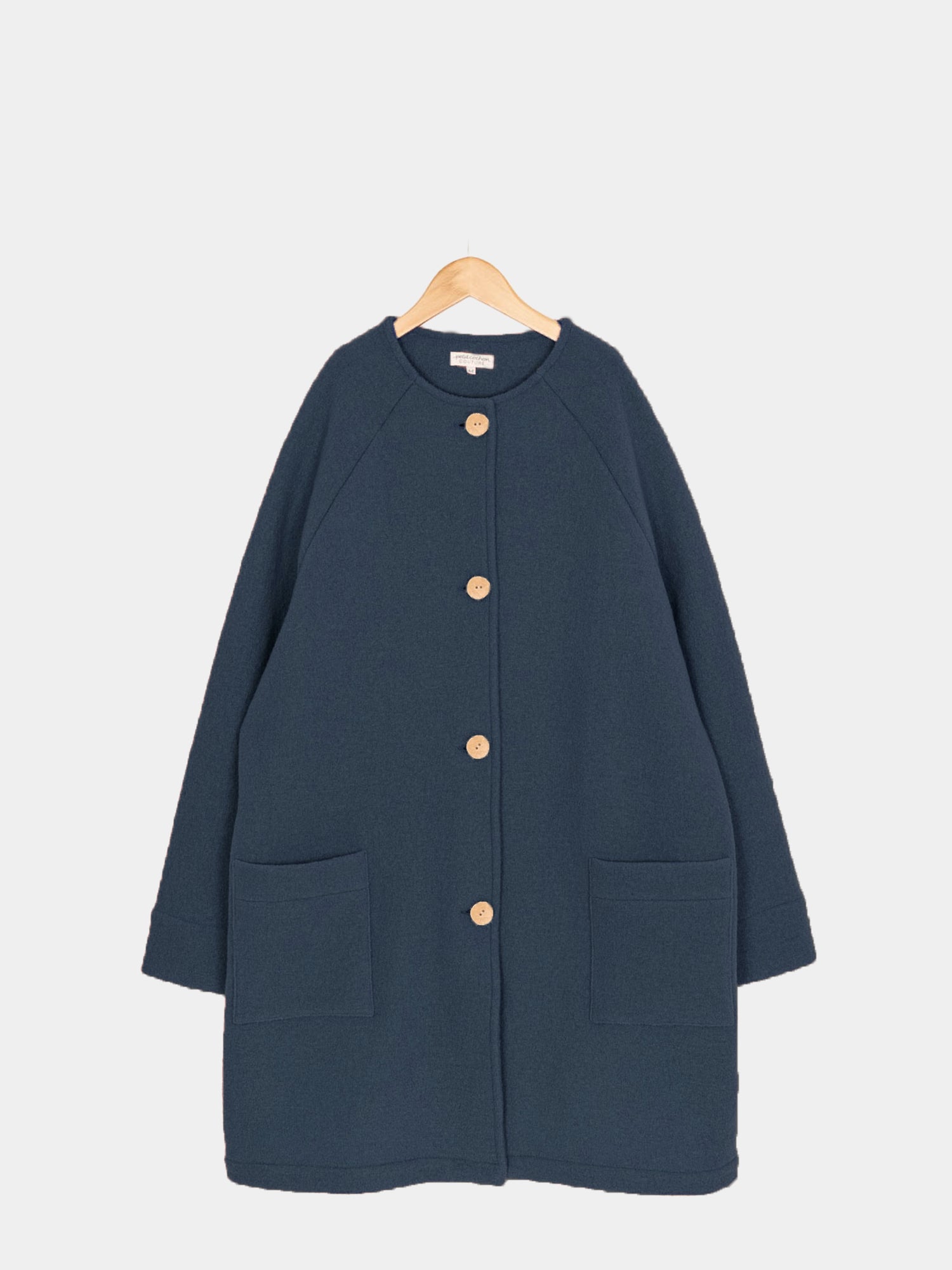 Wollmantel Damen - Marine: Navy-blauer, knielanger Wollmantel mit Rundhalsausschnitt, Raglanärmeln, vier Kokosknöpfen vorne und zwei Hüfttaschen, auf einem Holzkleiderbügel hängend.
