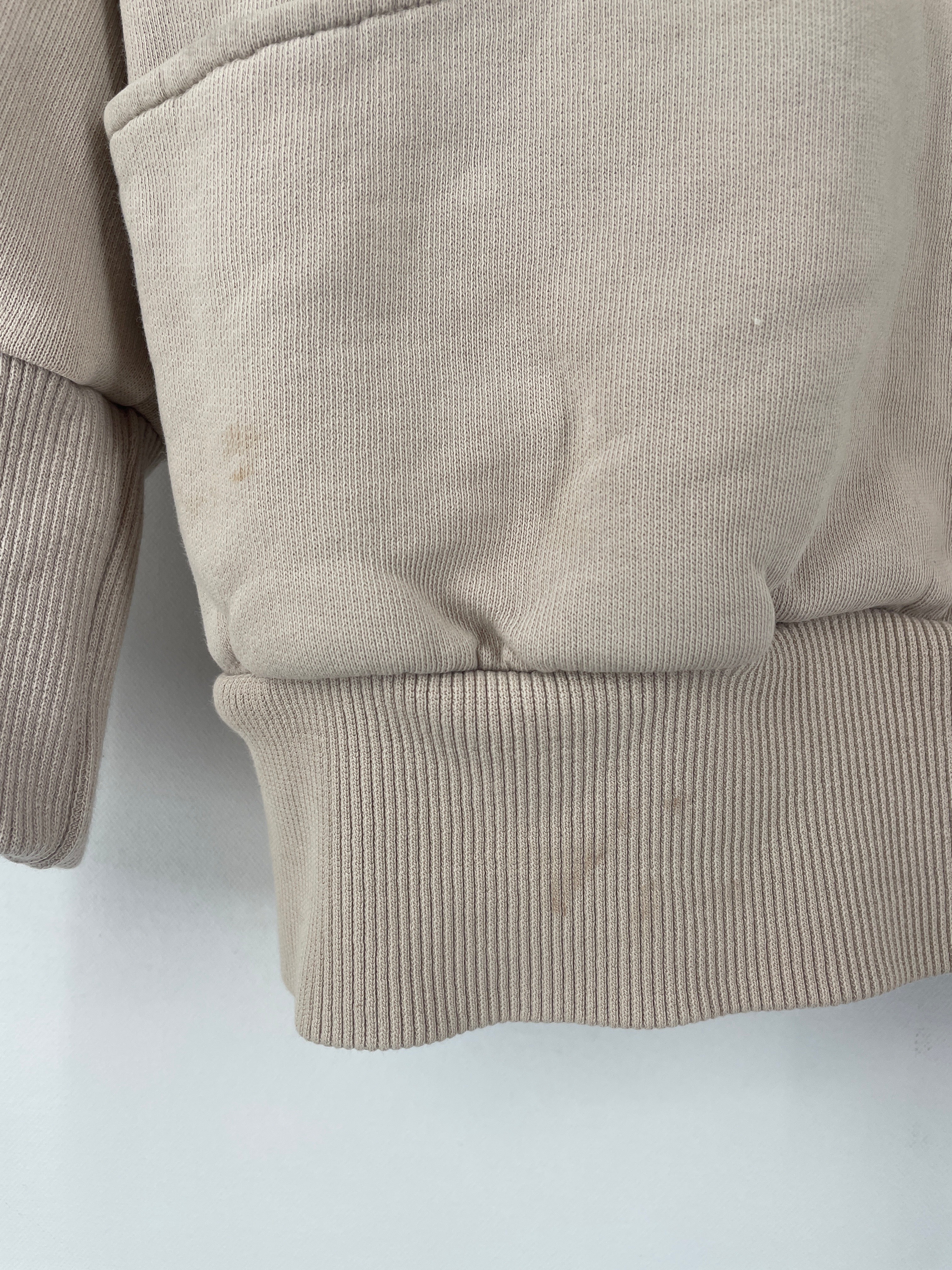 Nahaufnahme des Frauen Hoodie Sweat Sand Gr. S. Sichtbar sind der untere Rippbund, ein Teil der Kängurutasche und ein Ärmel. Leichte, braune Flecken sind auf dem Stoff erkennbar.