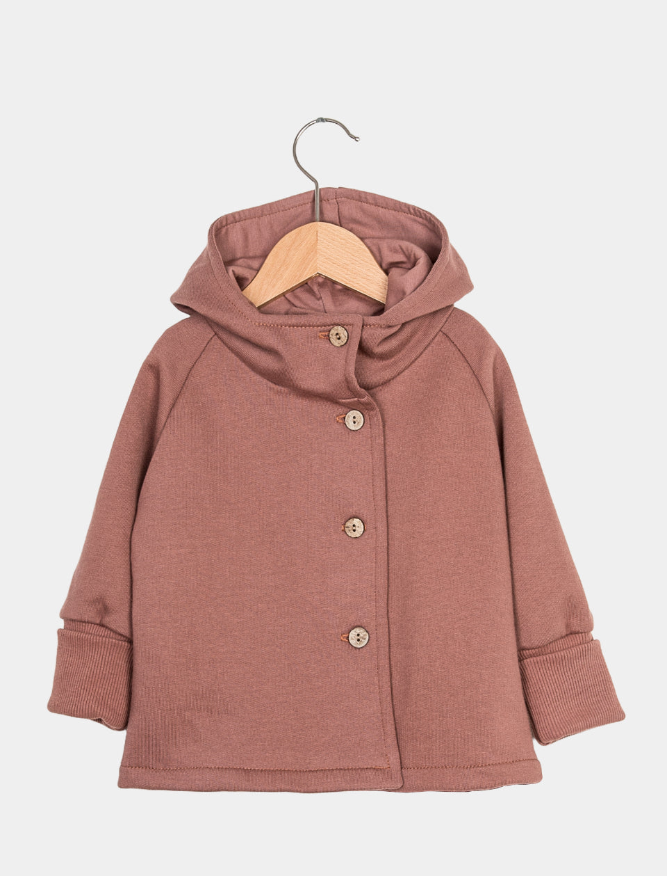 Die Wichteljacke Bio Sweat Zimt Gr 4/5Y zeigt eine Kapuzenjacke mit langen Ärmeln, umgeschlagenen Bündchen und vier kleinen Holzknöpfen, die an einem Holzkleiderbügel hängt.