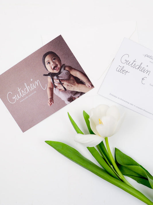 (Kopie) Geschenkgutschein: Zwei Gutscheinkarten, eine mit lächelndem Baby, eine zum Ausfüllen, neben einer weißen Tulpe. Einlösbar online und in Berlin-Tempelhof.