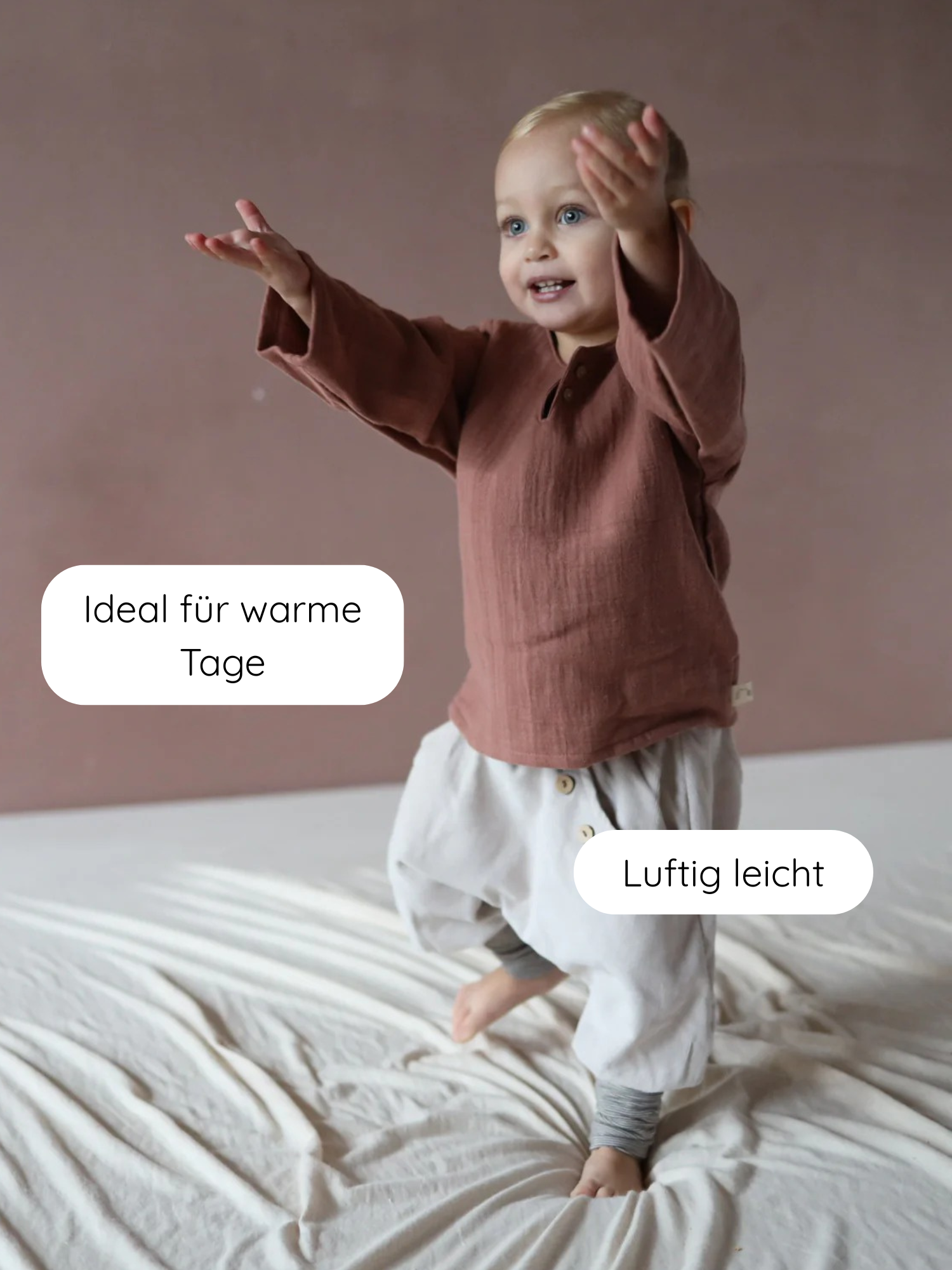 Kleinkind trägt Hemdchen Bio-Musselin - Zimt, steht auf hellem Stoff. Das langärmlige, luftige Oberteil mit lockerer Passform und Knopfleiste ist ideal für warme Tage, bietet Bewegungsfreiheit.