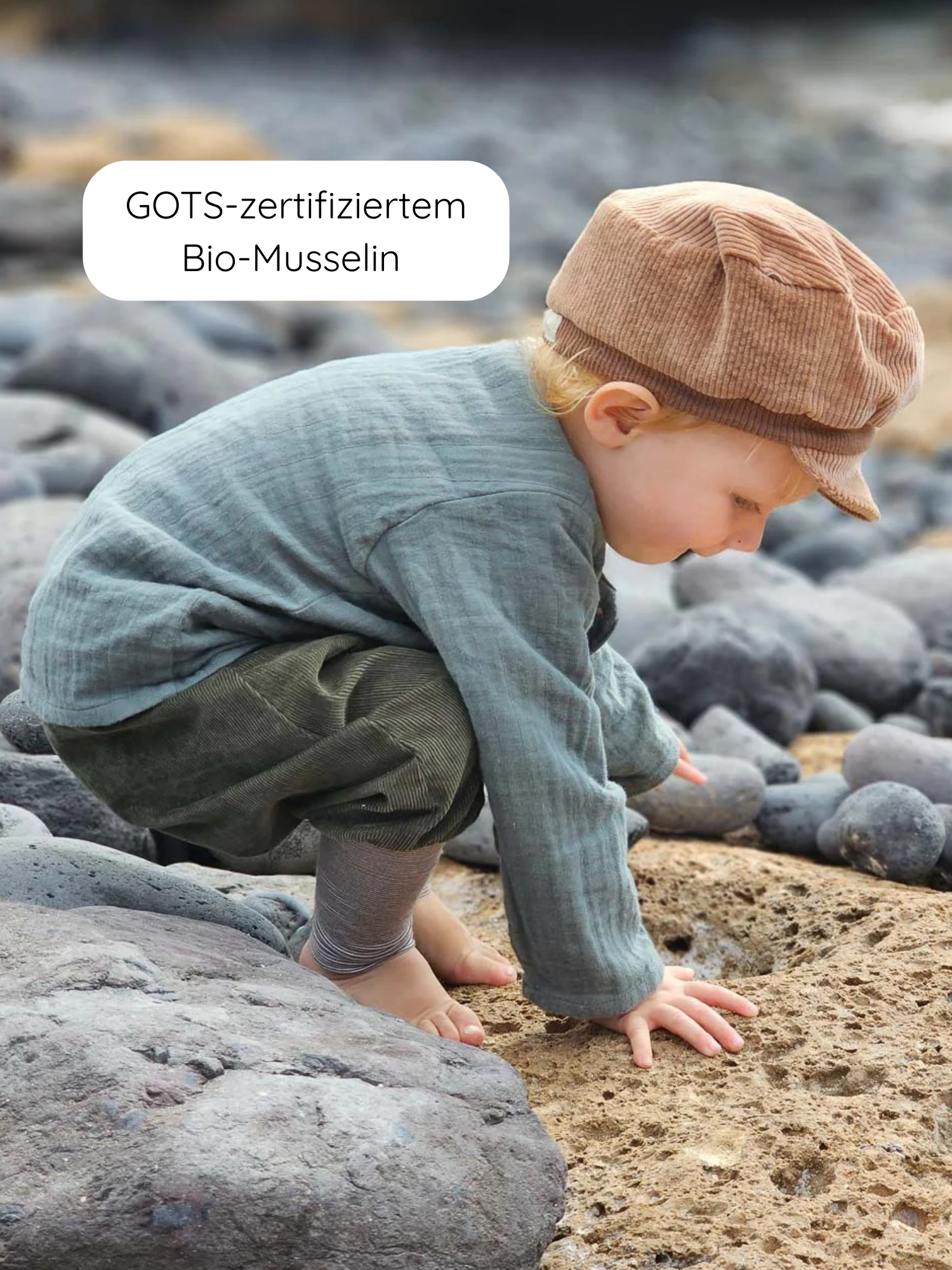 Kleinkind erkundet felsige Küste in GOTS-zertifiziertem Bio-Musselin Hemdchen Musselin - Eisblau. Das luftige, handgemachte Oberteil bietet Bewegungsfreiheit und Komfort, ideal für warme Tage.