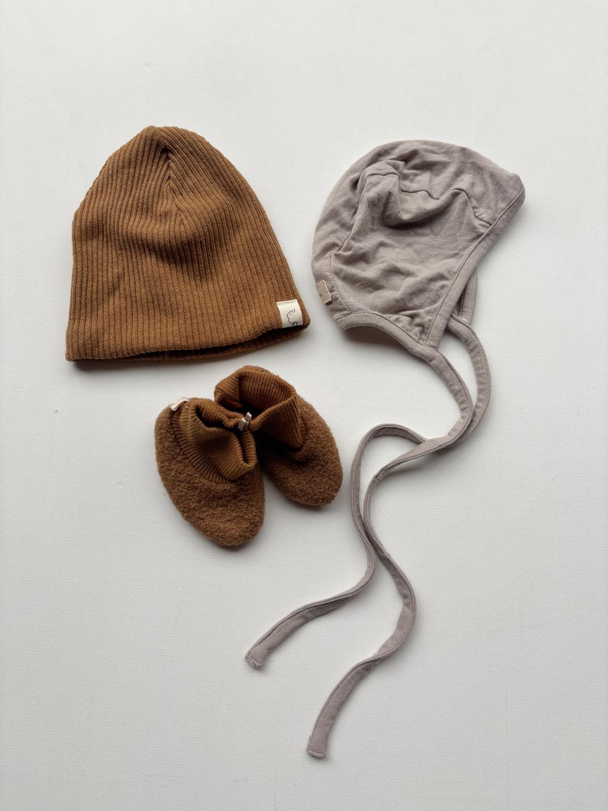 Set 5 Beanie, Schühchen und Häubchen in Gr Mini bis 0M: Eine braune Mütze, gestrickte Socken, und ein graues Häubchen, präsentiert auf einer weißen Fläche. Zustand: neu.