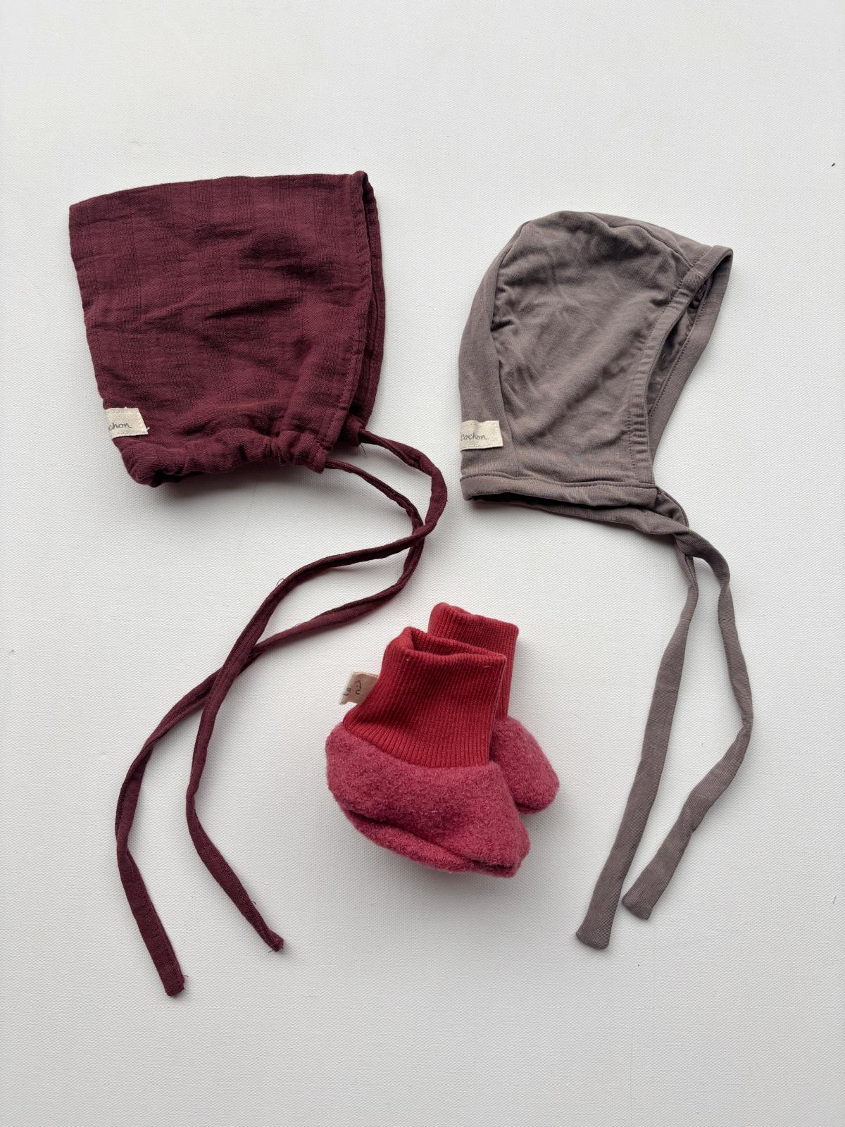 Set 10 Zwergenmütze, Schühchen und Häubchen in Gr 0M: Zwei Babymützen, Schühchen und Häubchen, sorgfältig arrangiert auf einer weißen Oberfläche. Perfekt für Neugeborene, ideal für gemütliche und stilvolle Momente.