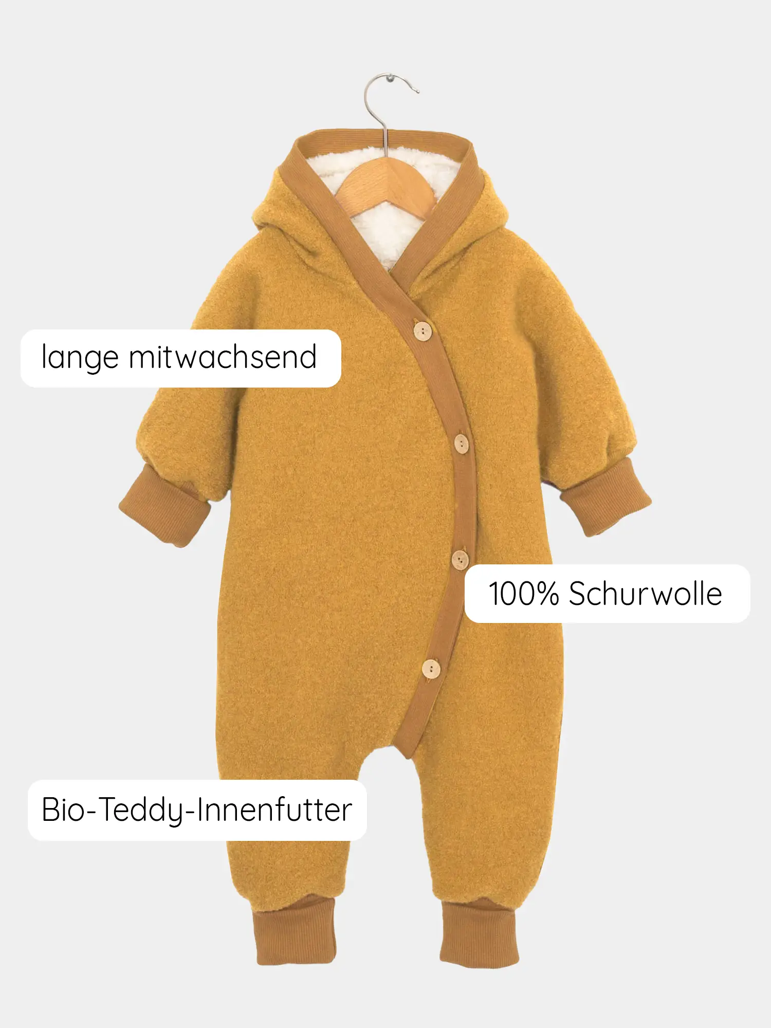 Teddy-Kuschelanzug Wollwalk - Honig, ein senfgelber Baby-Overall mit Kapuze, Holzknöpfen und Bio-Teddy-Innenfutter, das auf einem Holzkleiderbügel hängt, für kalte Wintertage geeignet.