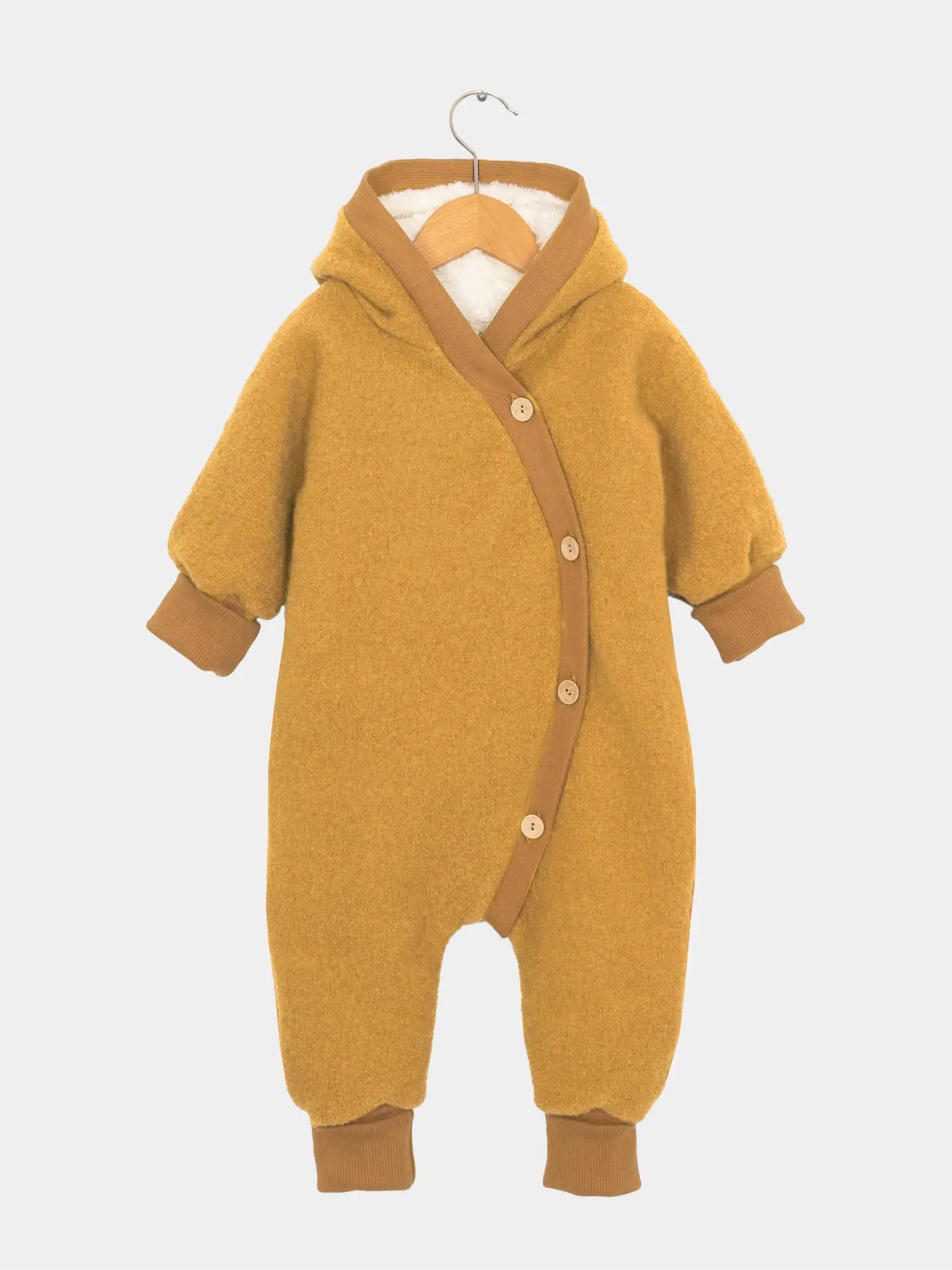 Der Teddy-Kuschelanzug Wollwalk - Honig zeigt einen weichen, senfgelben Overall mit Holzknöpfen und Kapuze, gefertigt aus Bio-Wolle und -Baumwolle, ideal für Wintertage.