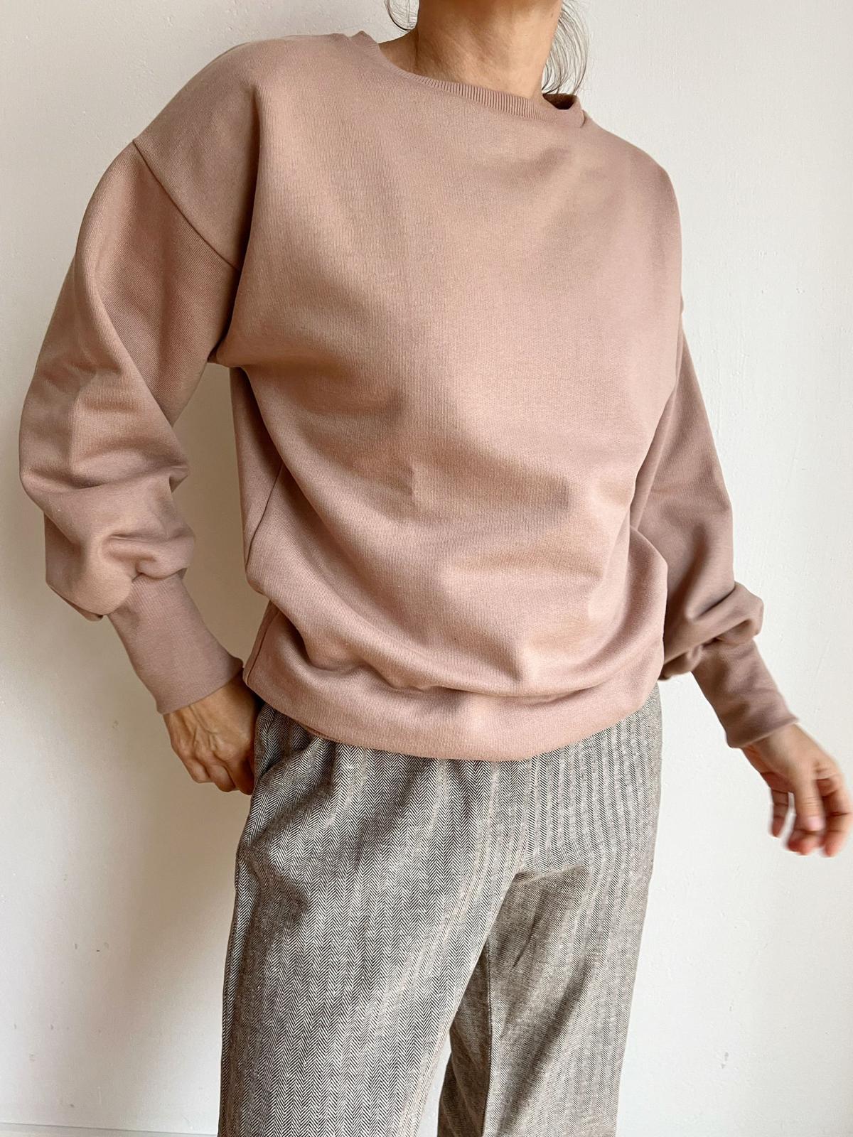 Nahaufnahme einer Person, die den Frauen Pumppulli aus Bio-Baumwolle - Puder trägt. Der lockere Schnitt mit überschnittenen Schultern verleiht dem Look eine moderne Silhouette und maximalen Komfort.