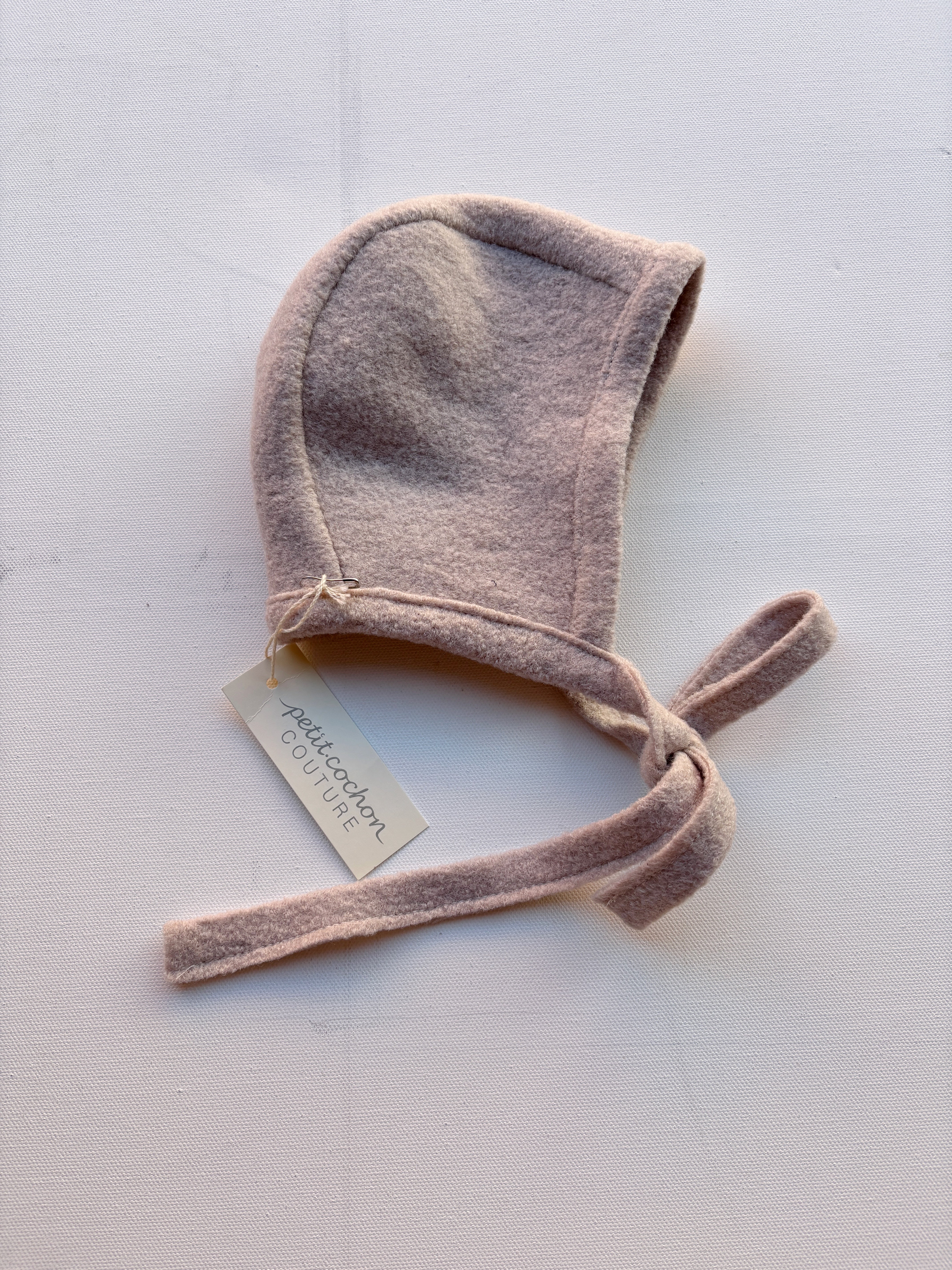 Baby Häubchen Wollwalk Sand Gr. 6M, gestrickt mit einem Tag, gefüttert mit Bio-Jersey. Zeigt ein modisches Accessoire mit detaillierten Stichen und einer weißen Etikette mit silberner Schrift.