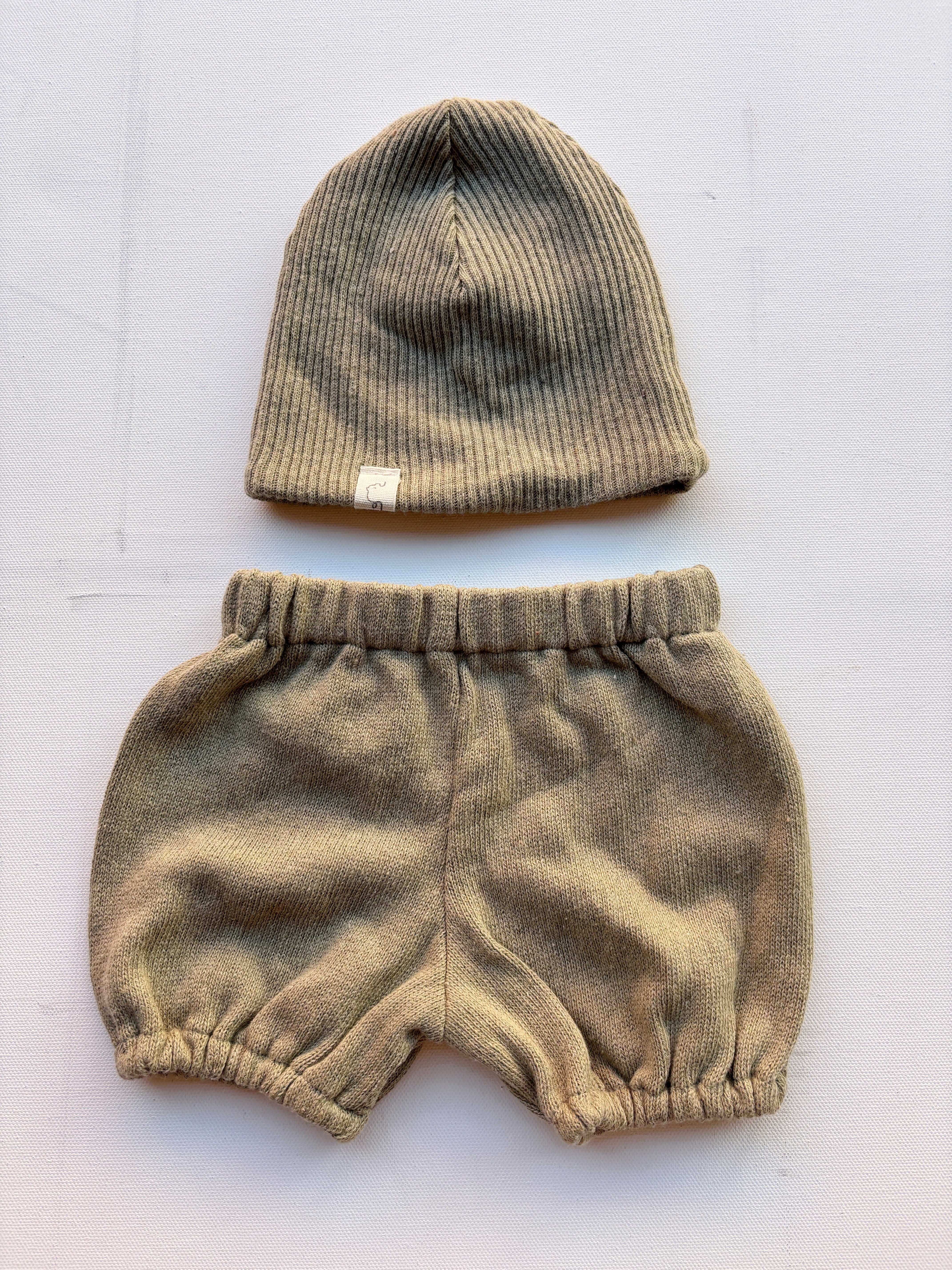 Baby Set Beanie & Pumphose aus Bio-Baumwollstrick in Salbei, bestehend aus einer gestrickten Mütze und einer Hose, auf einer weißen Fläche präsentiert. Zustand: neu.