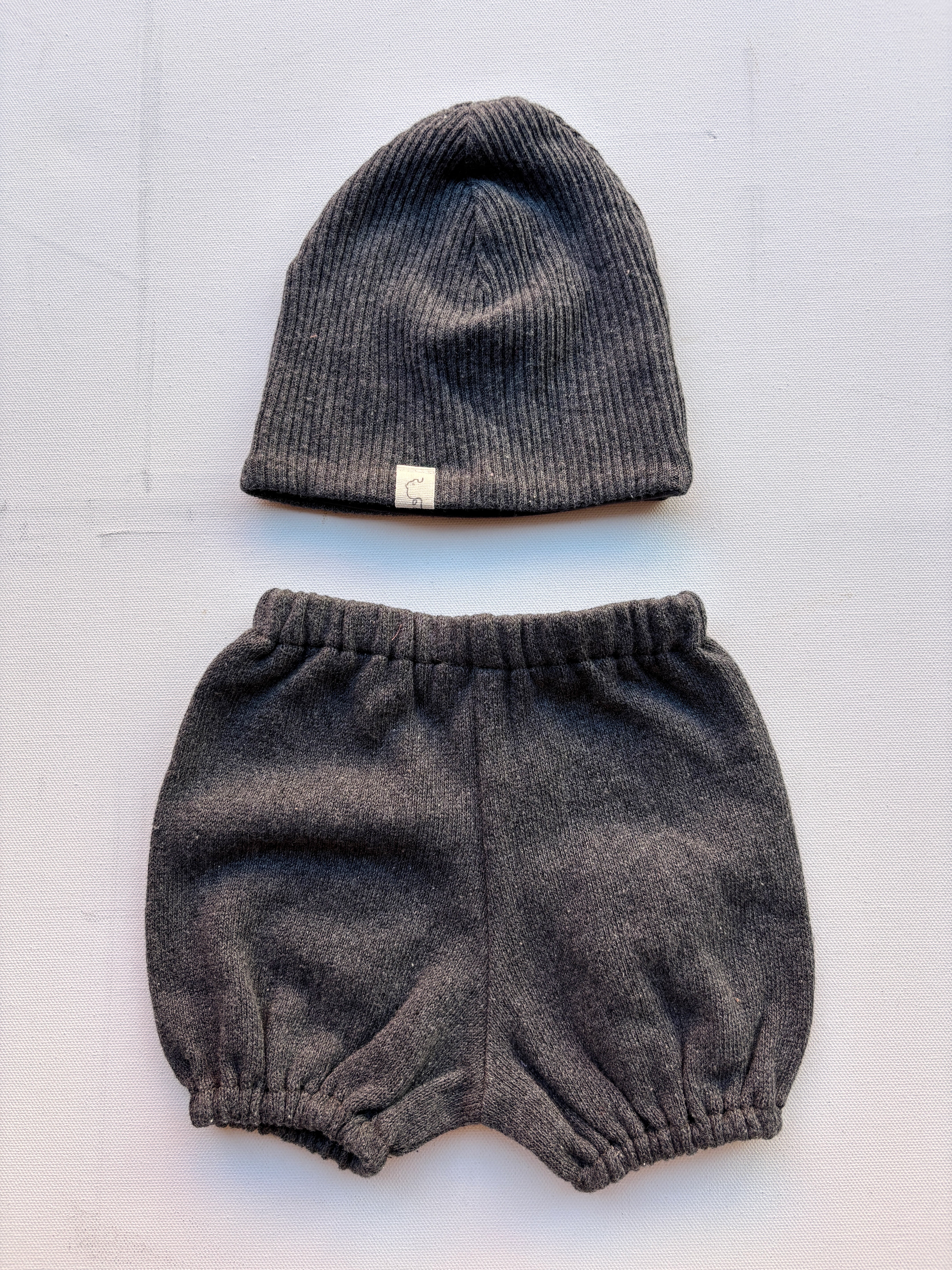 Baby Set Beanie & Pumphose Bio-Baumwollstrick Ruß Gr. 0M, bestehend aus einer gestrickten Mütze mit weißem Label und einer dazu passenden Pumphose, auf einer weißen Fläche arrangiert.