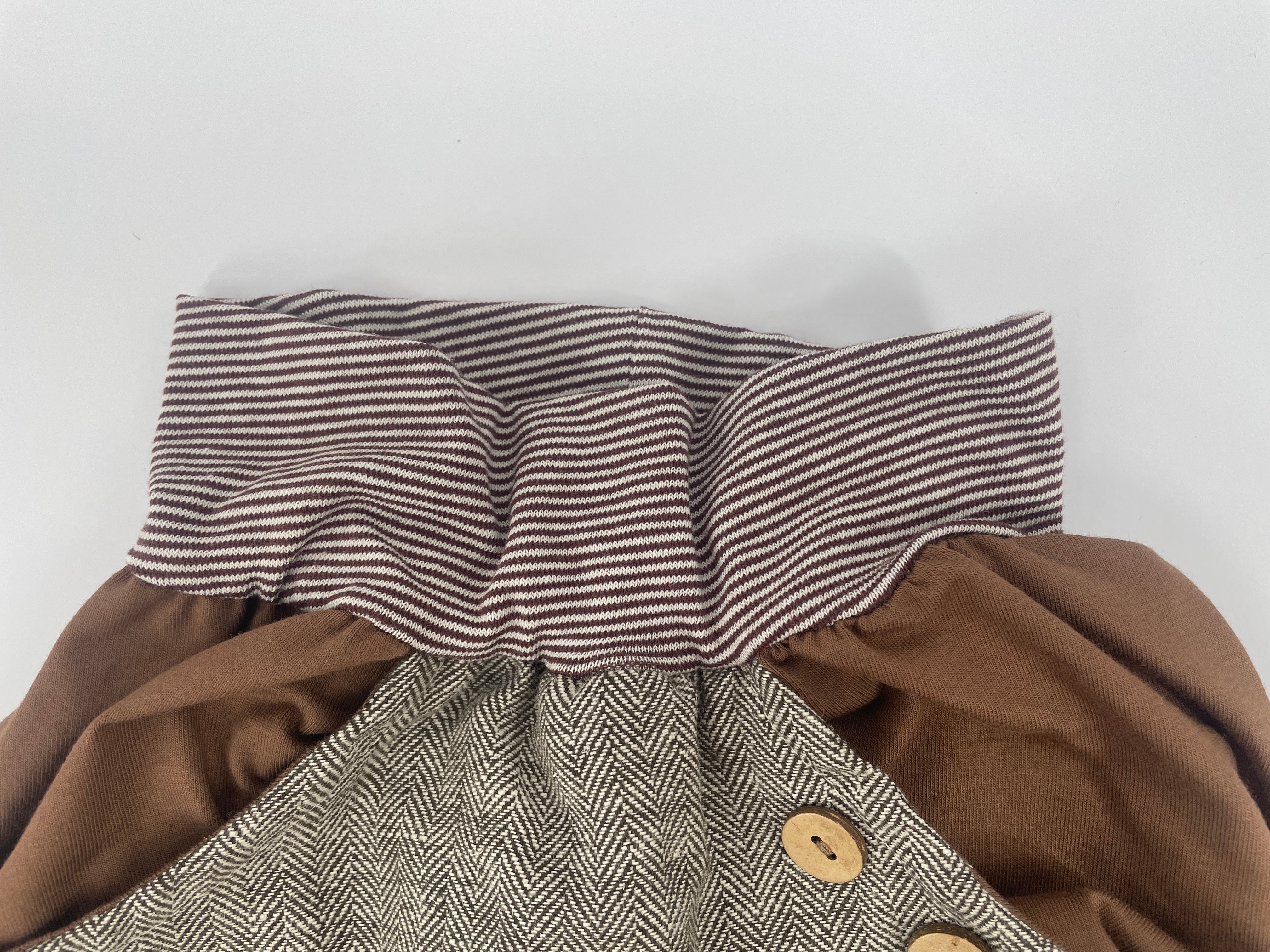 Kurze Knickerbocker Fischgrat Nougat Gr. 1 mit detailreichem Fischgratmuster, braunem Ringel-Bündchen und präziser Strickarbeit, zeigt hochwertige Verarbeitung durch Nahaufnahmen von Stoff und Knopf. Zustand: neu.