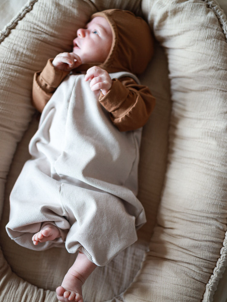 Neugeborenes in einem weichen Baby-Lounger, trägt eine Kurze Baby Schlupflatzhose Feincord - Sand, die bequem und ohne Verschlüsse ist, perfekt für einfaches Anziehen.
