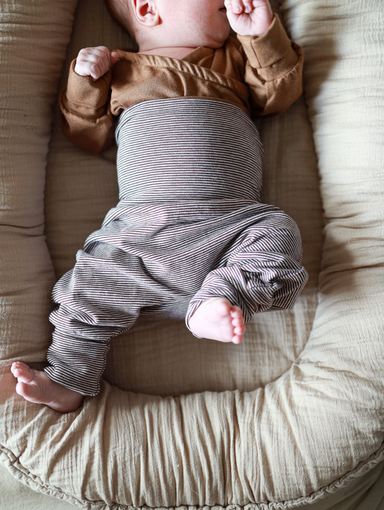 Baby trägt Babyknicker Bio-Baumwolle - Schoko Ringel, liegt entspannt in einem gepolsterten Baby-Lounger. Die Hose bietet Bewegungsfreiheit und ist sanft zur Haut, ideal für den täglichen Gebrauch.