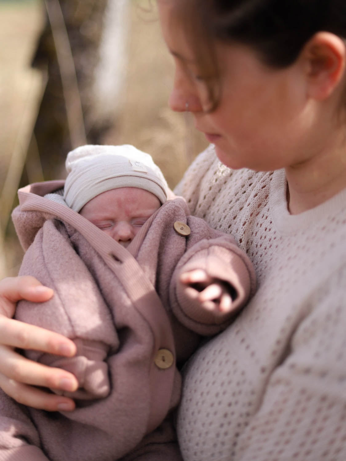 Frau hält Baby im Kuschelanzug Wollwalk - Puder, ideal für Tragetuch, mit langen Bündchen für Wärme und Bewegungsfreiheit.