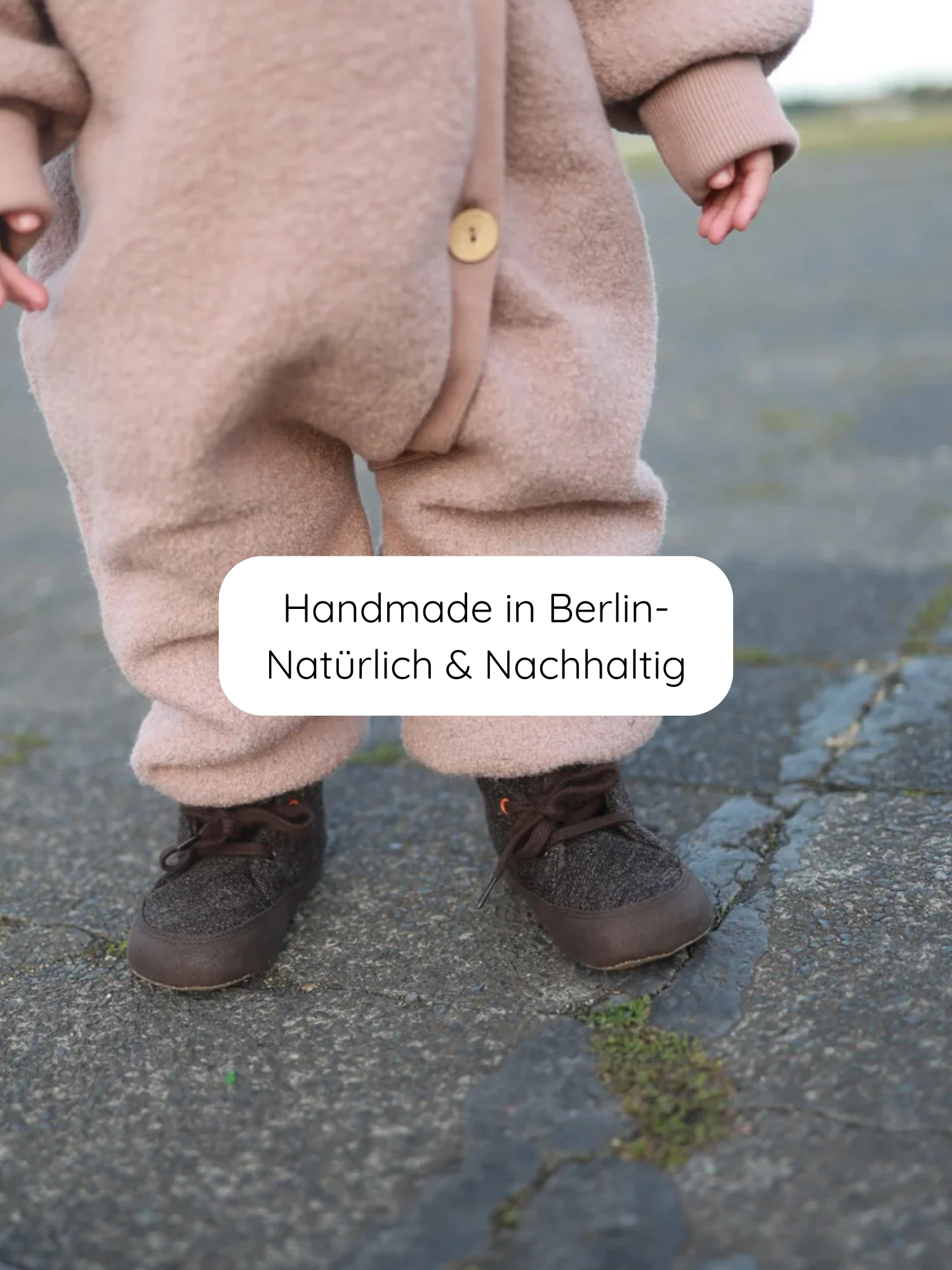 Kleinkind in Kuschelanzug Wollwalk - Puder aus 100% Schurwolle, mit Baumwollfutter. Der Anzug hat Krempelbündchen und bietet Bewegungsfreiheit. Handgefertigt in Berlin, kombiniert mit Wollfilz-Booties.