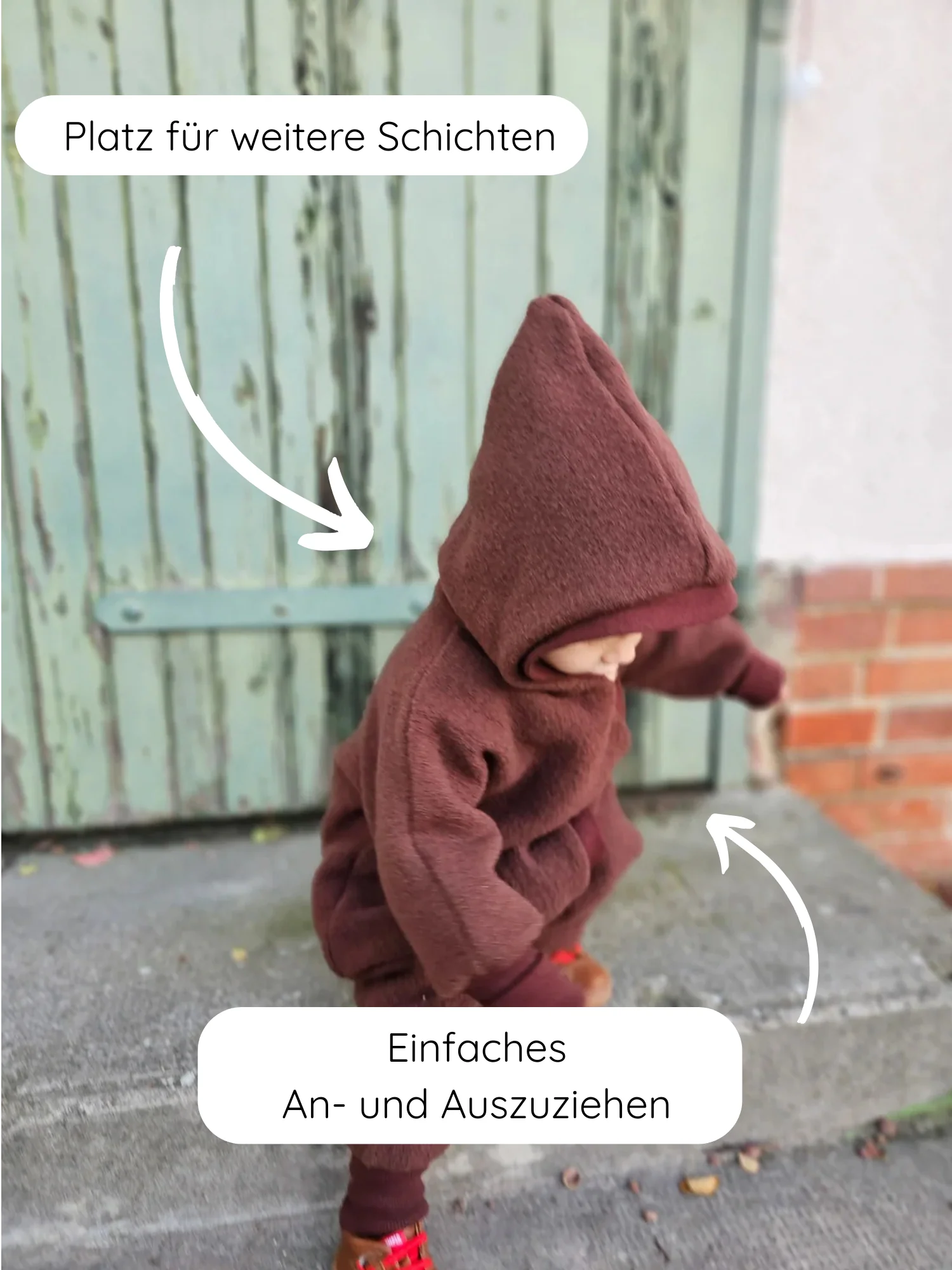 Kleinkind trägt den Kuschelanzug Wollwalk - Schoko, einen warmen, einteiligen Anzug mit Kapuze, der leicht an- und auszuziehen ist. Platz für zusätzliche Schichten, ideal für kühle Tage.